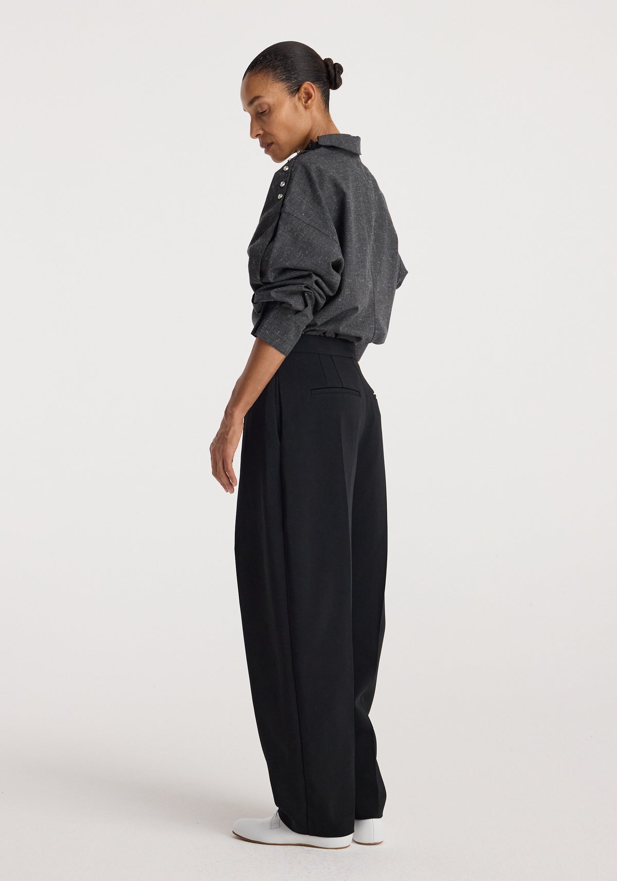 Woman wearing a grey slub textured Reimagined collar top with long sleeves and button details on the shoulder, paired with high-waisted black wide-leg pants and white shoes.