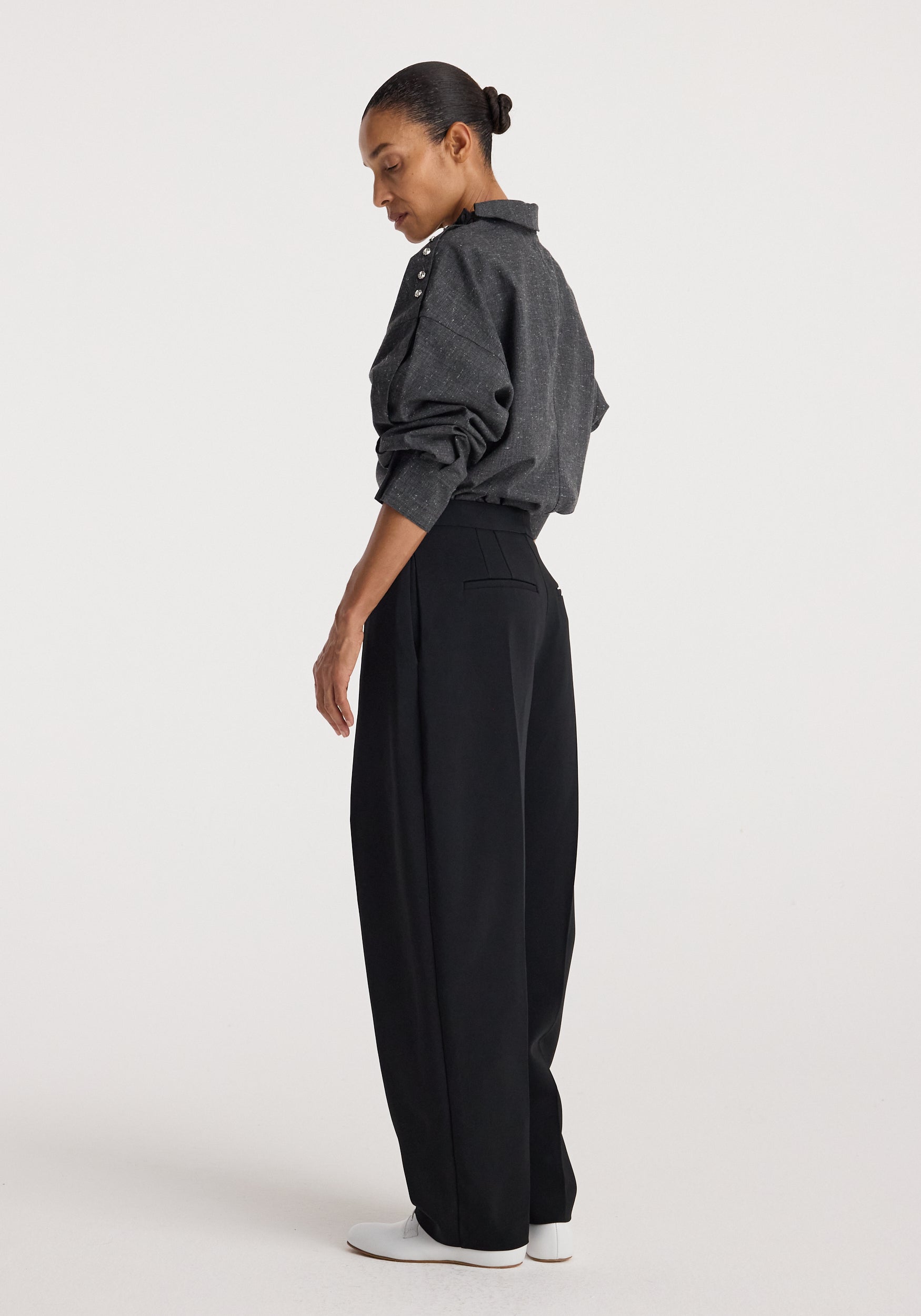 Woman wearing a grey slub textured Reimagined collar top with long sleeves and button details on the shoulder, paired with high-waisted black wide-leg pants and white shoes.