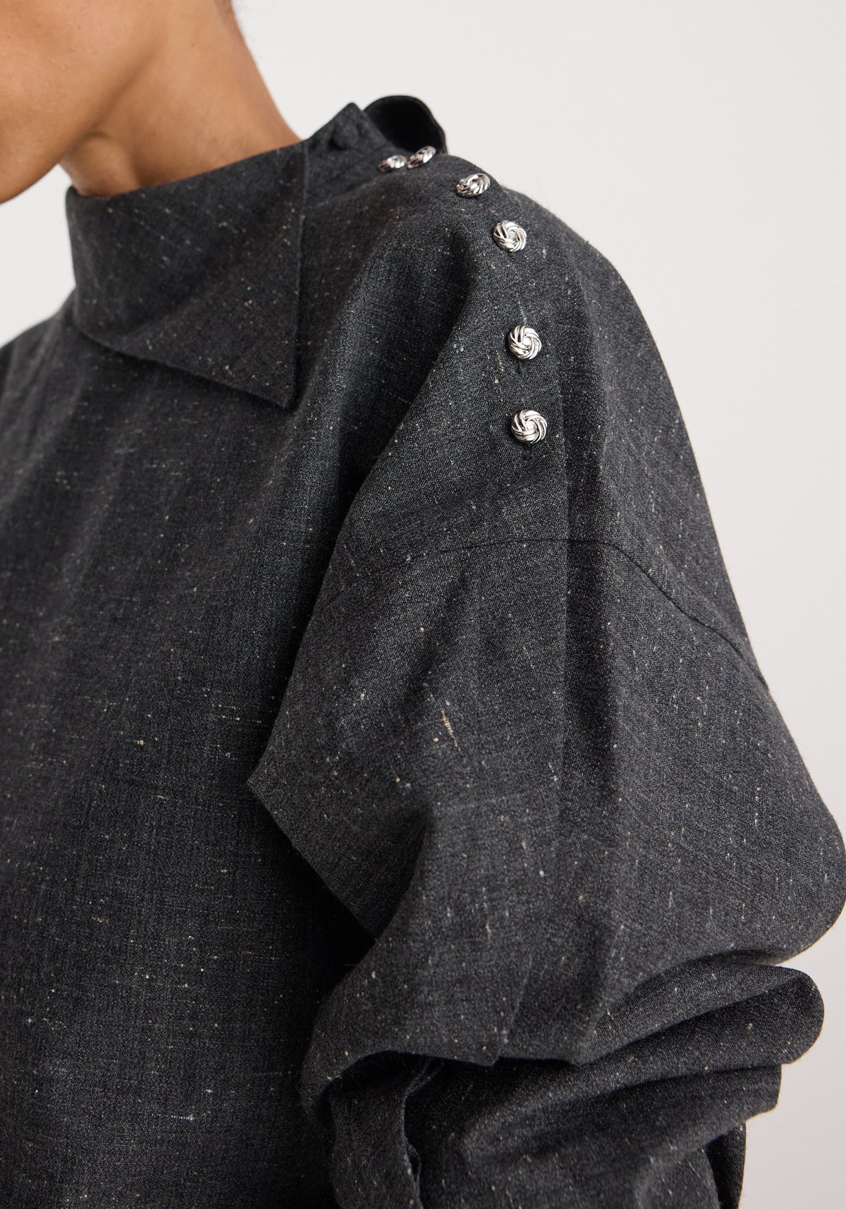 Close-up of a grey textured fabric with a high, structured collar and decorative silver buttons along the shoulder on the Reimagined collar top | grey slub.