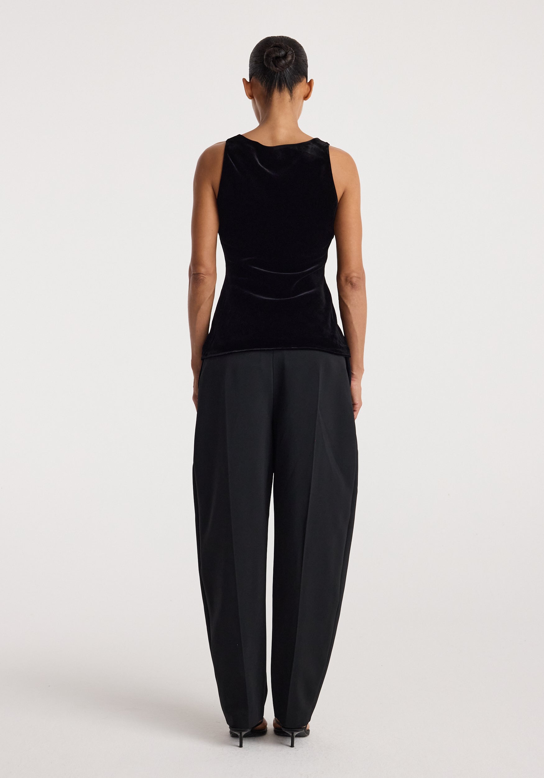 Woman seen from behind wearing a black scoop-neck silk velvet top | black paired with loose black trousers and black heels against a plain background.