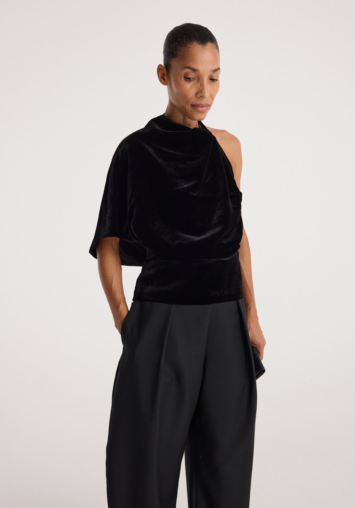 Draped open back silk velvet top | black, modeled in a draped silhouette with an exposed shoulder and wide-leg black trousers against a neutral background