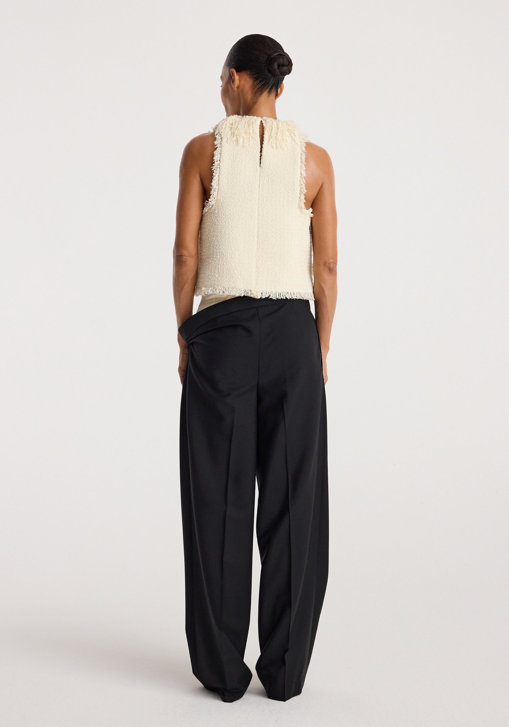 Woman seen from behind wearing a cream sleeveless textured fringe bouclé top with a keyhole back, paired with loose black wide-leg trousers against a plain background