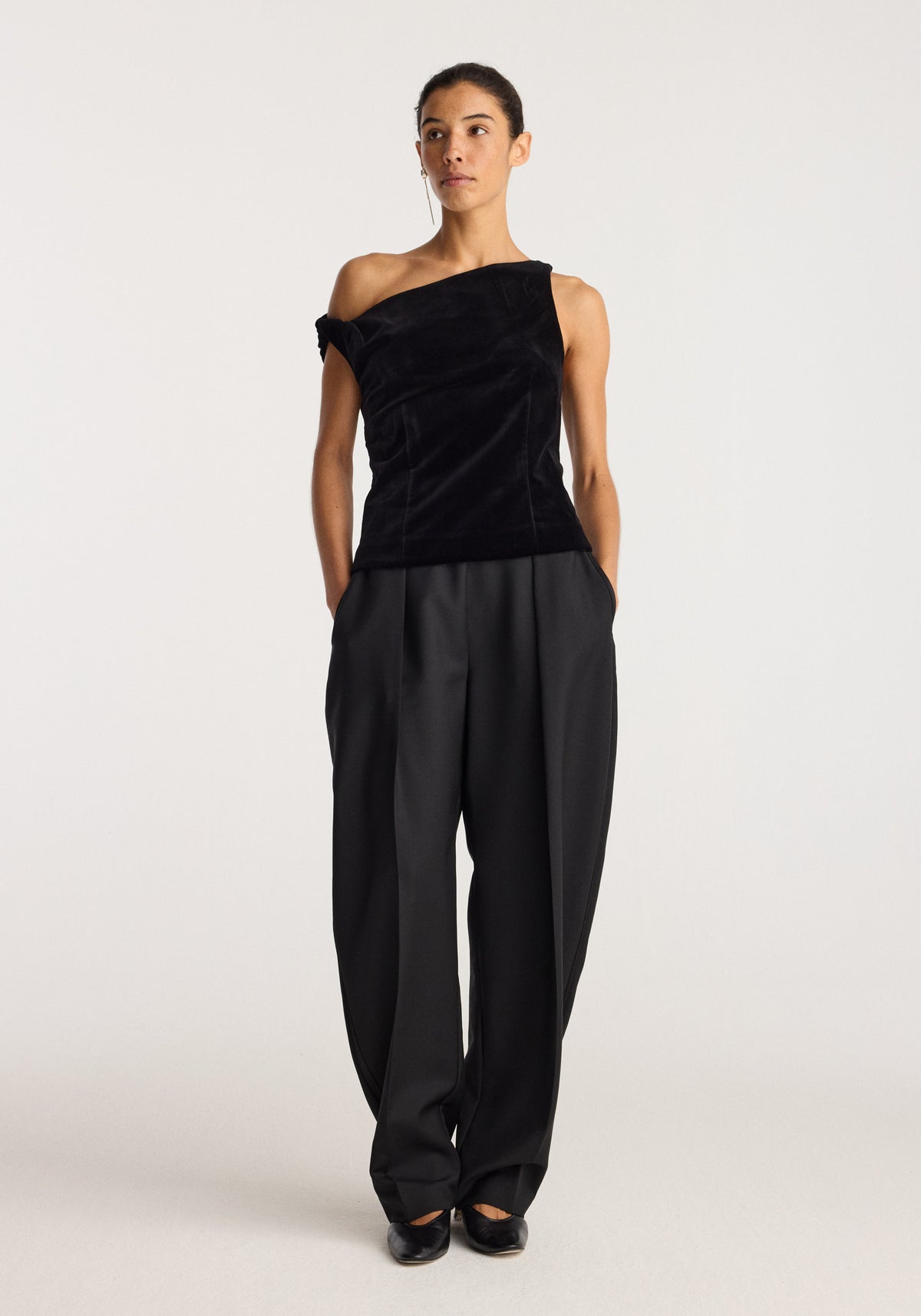 Draped velvet top | black with an asymmetrical neckline styled with wide leg black trousers on a model