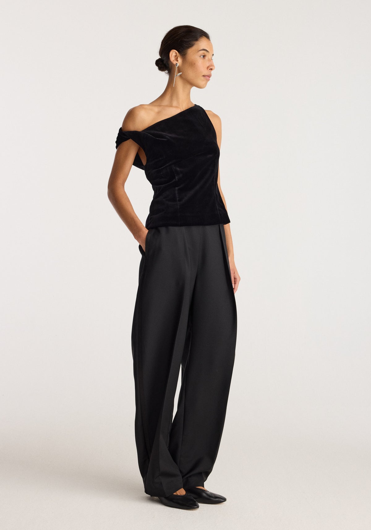Draped velvet top | black shown on a model with an asymmetric neckline and gathered draping, paired with wide leg black trousers