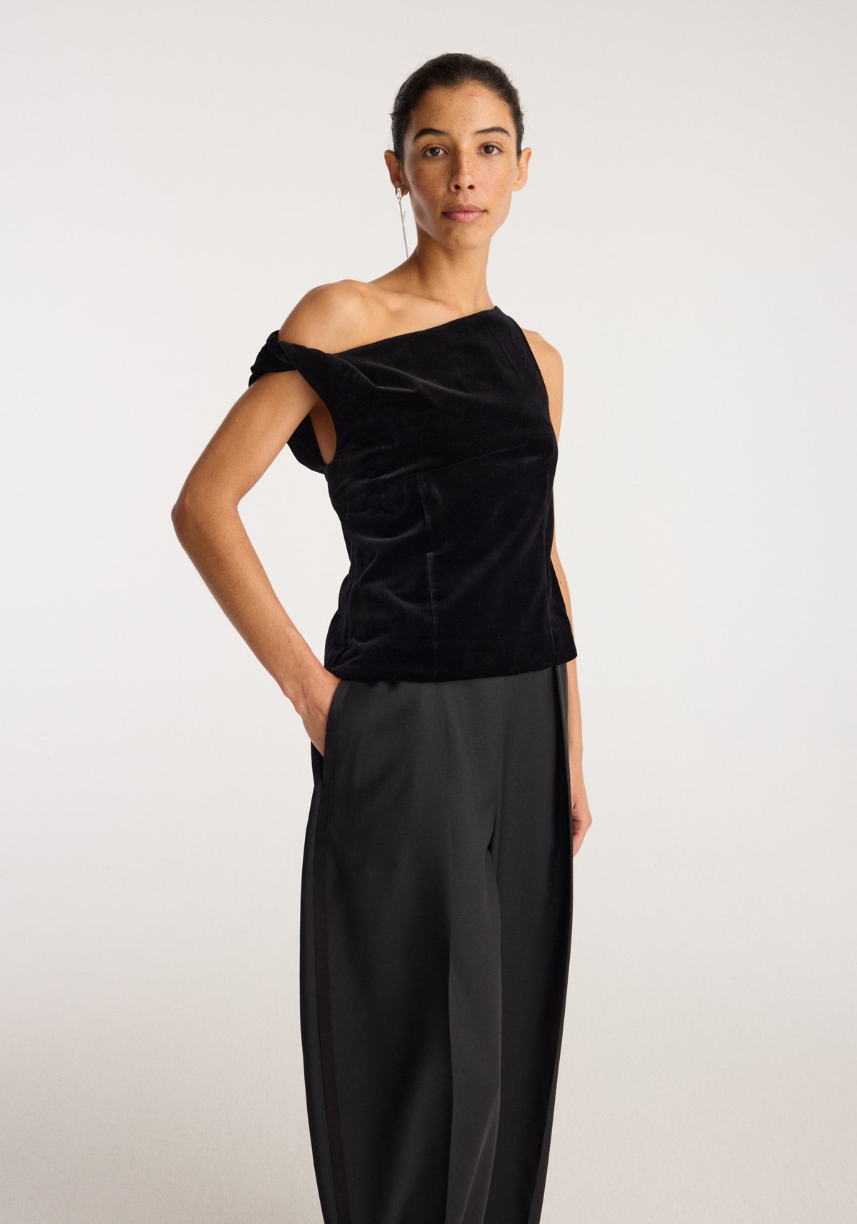 Draped velvet top | black worn by a model with an asymmetric neckline and softly gathered draping paired with wide leg black trousers