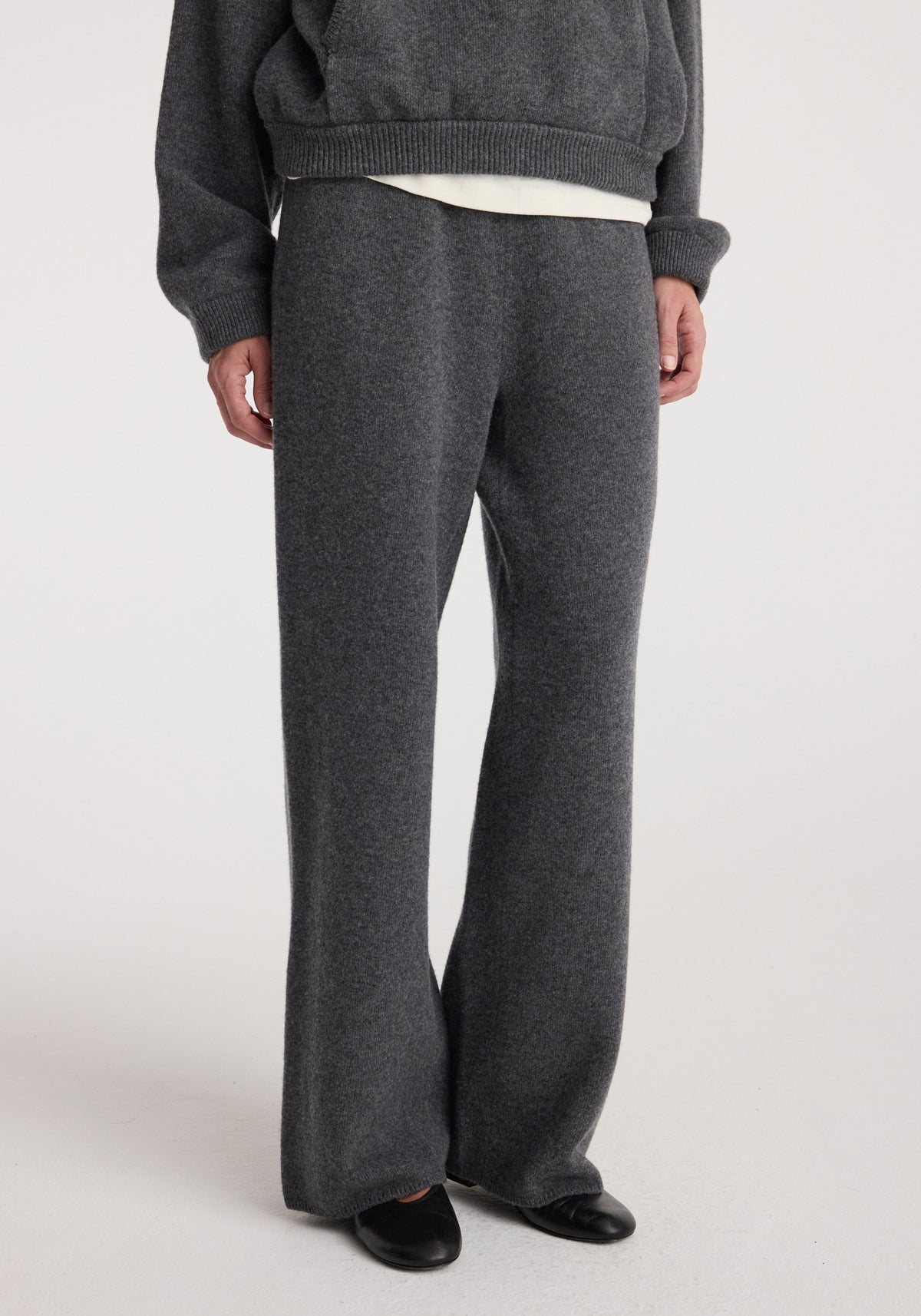 Person wearing dark grey melange Compact knitted trousers paired with a matching sweater and black shoes, standing against a plain light background.
