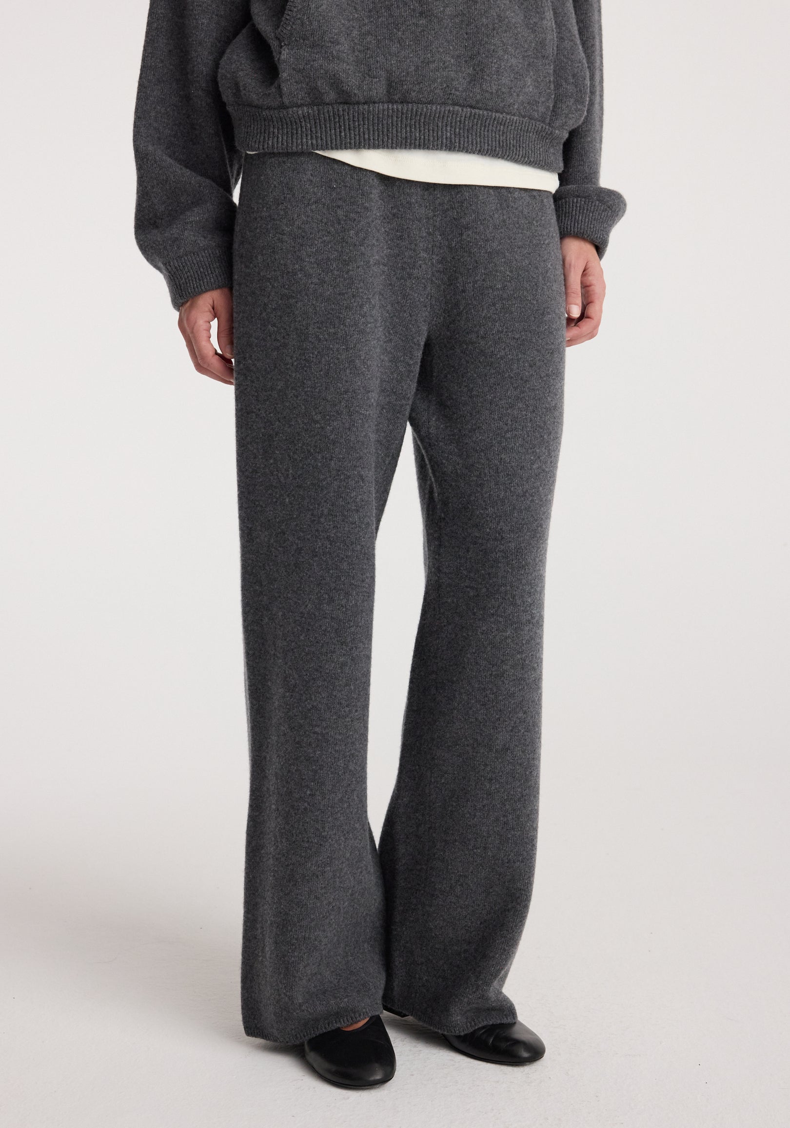Person wearing dark grey melange Compact knitted trousers paired with a matching sweater and black shoes, standing against a plain light background.
