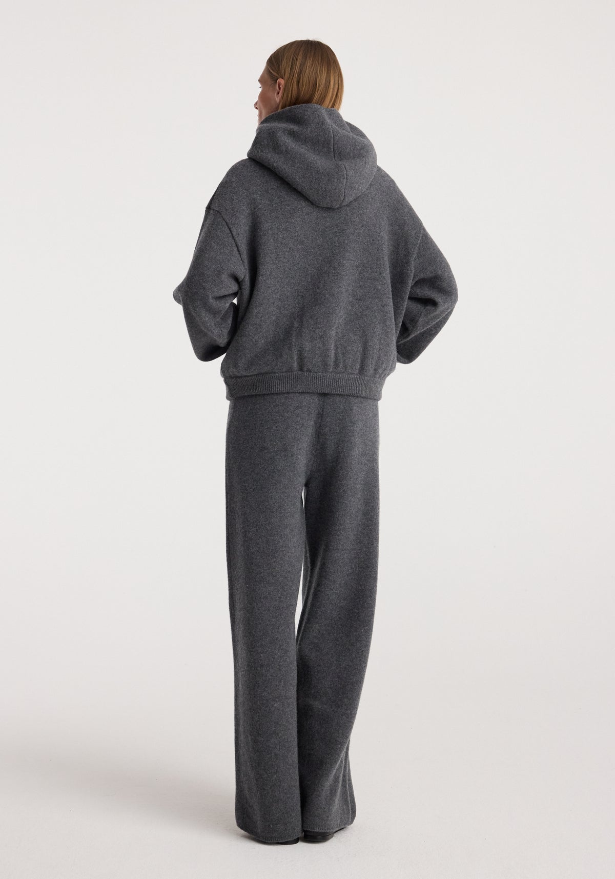 Rear view of a person wearing dark grey melange loose-fit knitwear including Compact knitted trousers | dark grey melange, paired with a matching hoodie.
