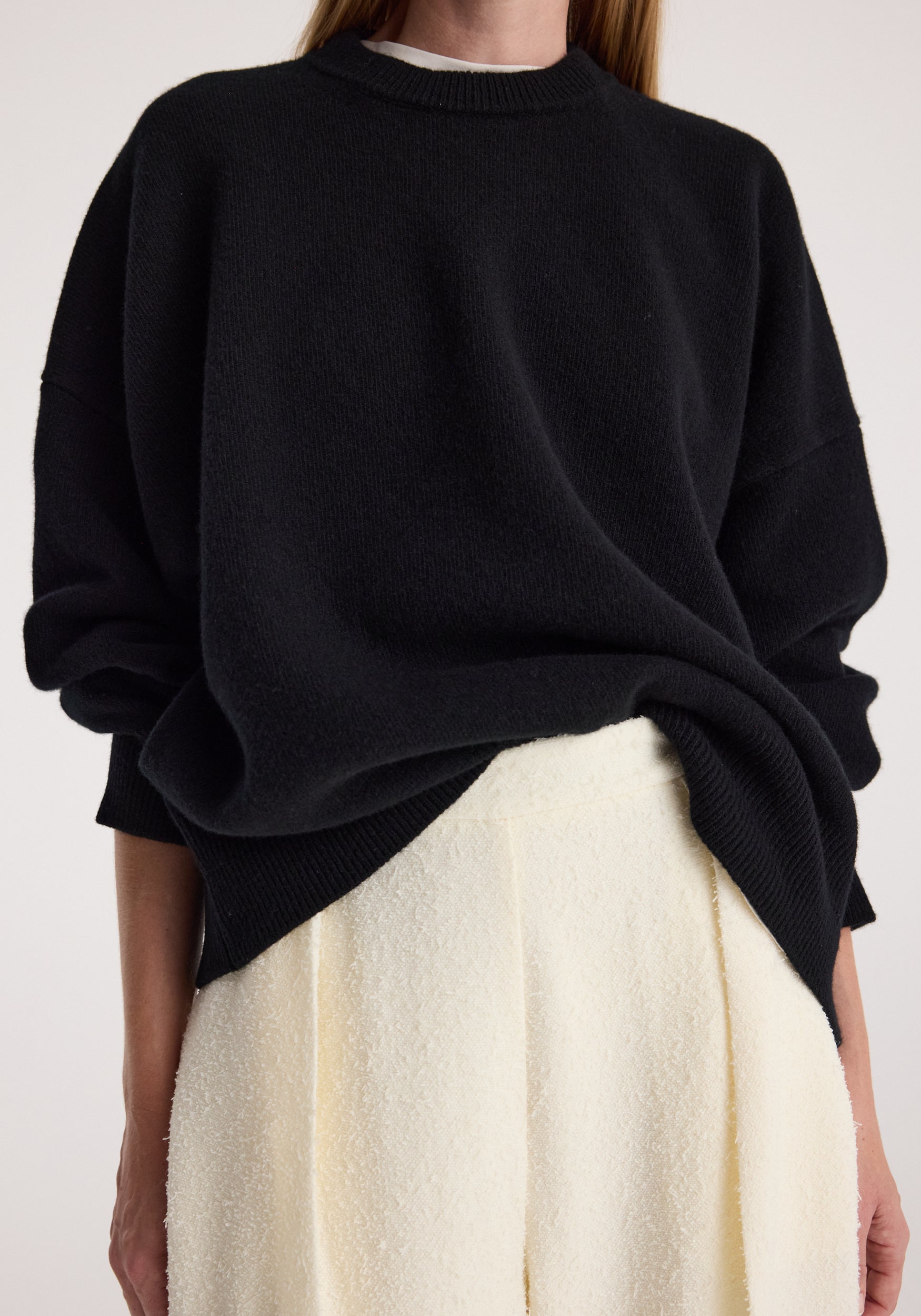 Person wearing a loose fit Classic crewneck jumper | black paired with high-waisted, textured cream pants against a neutral background.