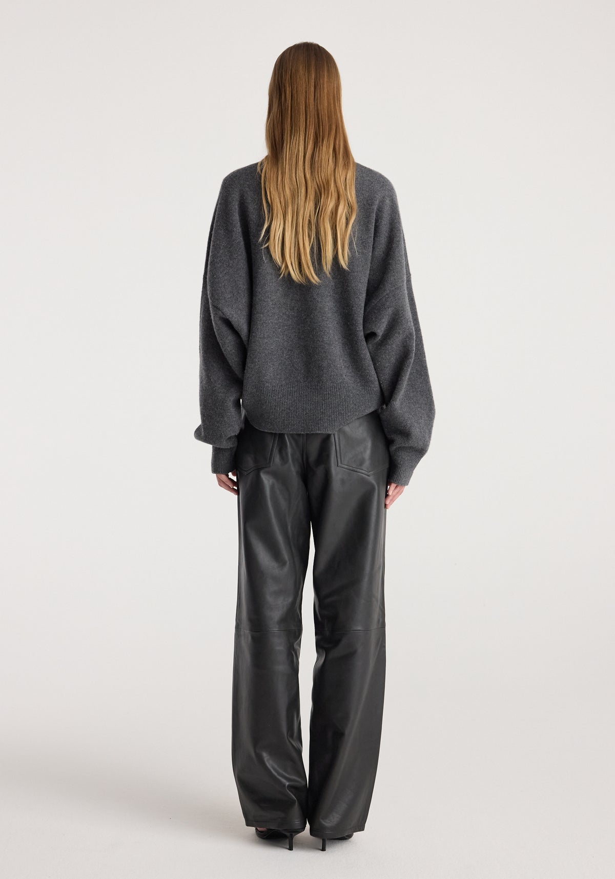Rear view of a person wearing a Classic crewneck jumper | dark grey melange paired with black leather wide-leg pants against a plain light background.