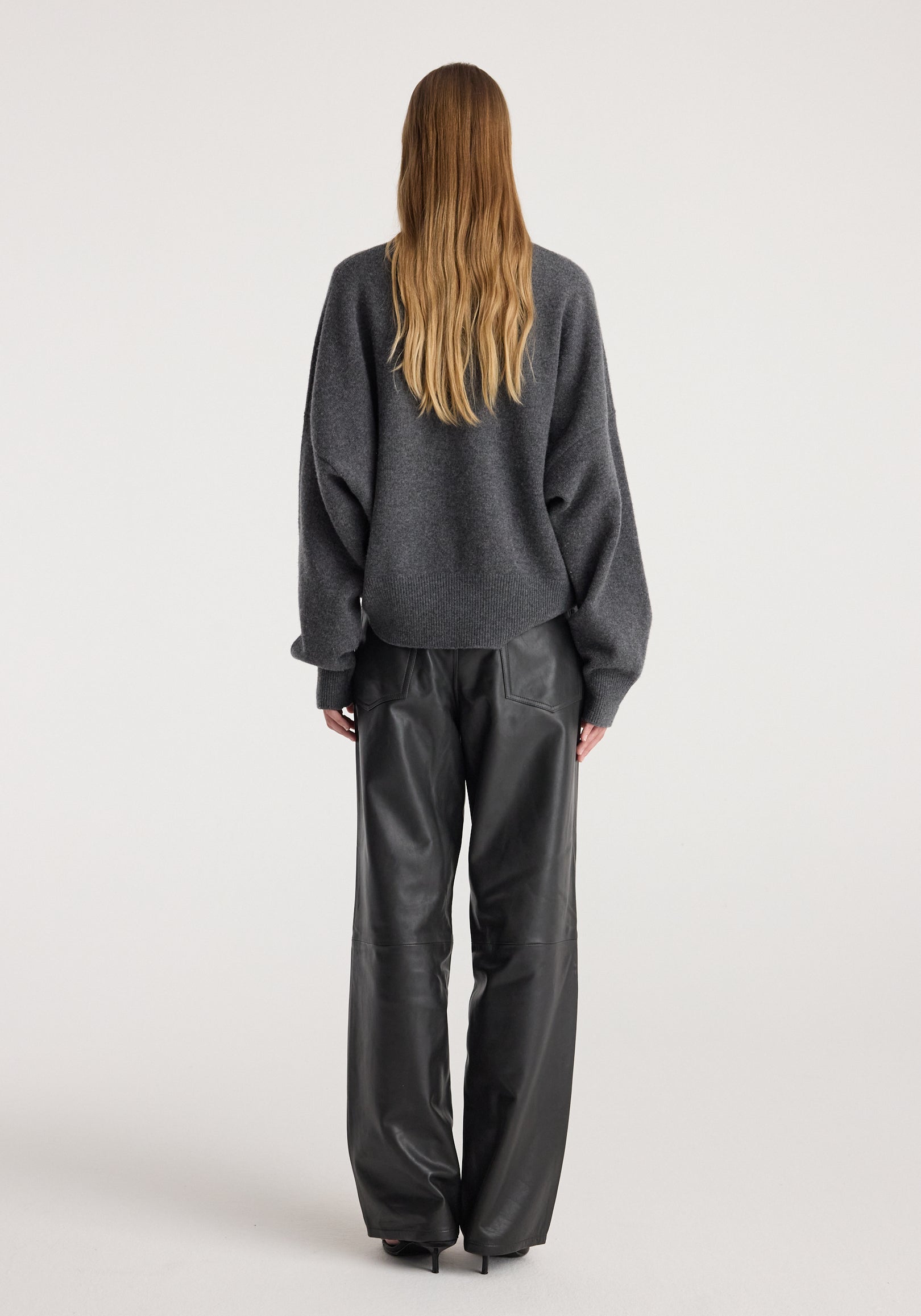 Rear view of a person wearing a Classic crewneck jumper | dark grey melange paired with black leather wide-leg pants against a plain light background.