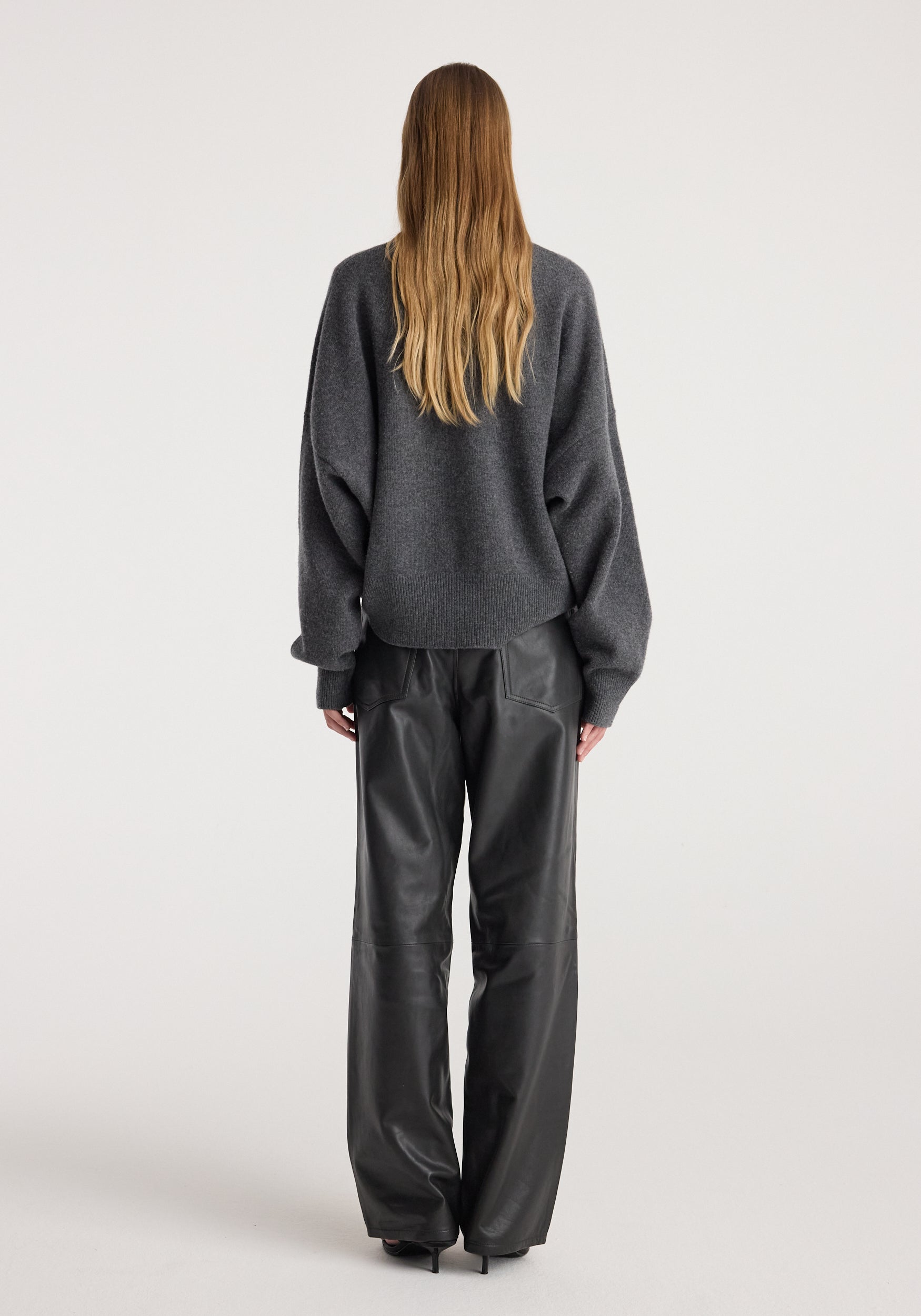 Rear view of a person wearing a Classic crewneck jumper | dark grey melange paired with black leather wide-leg pants against a plain light background.