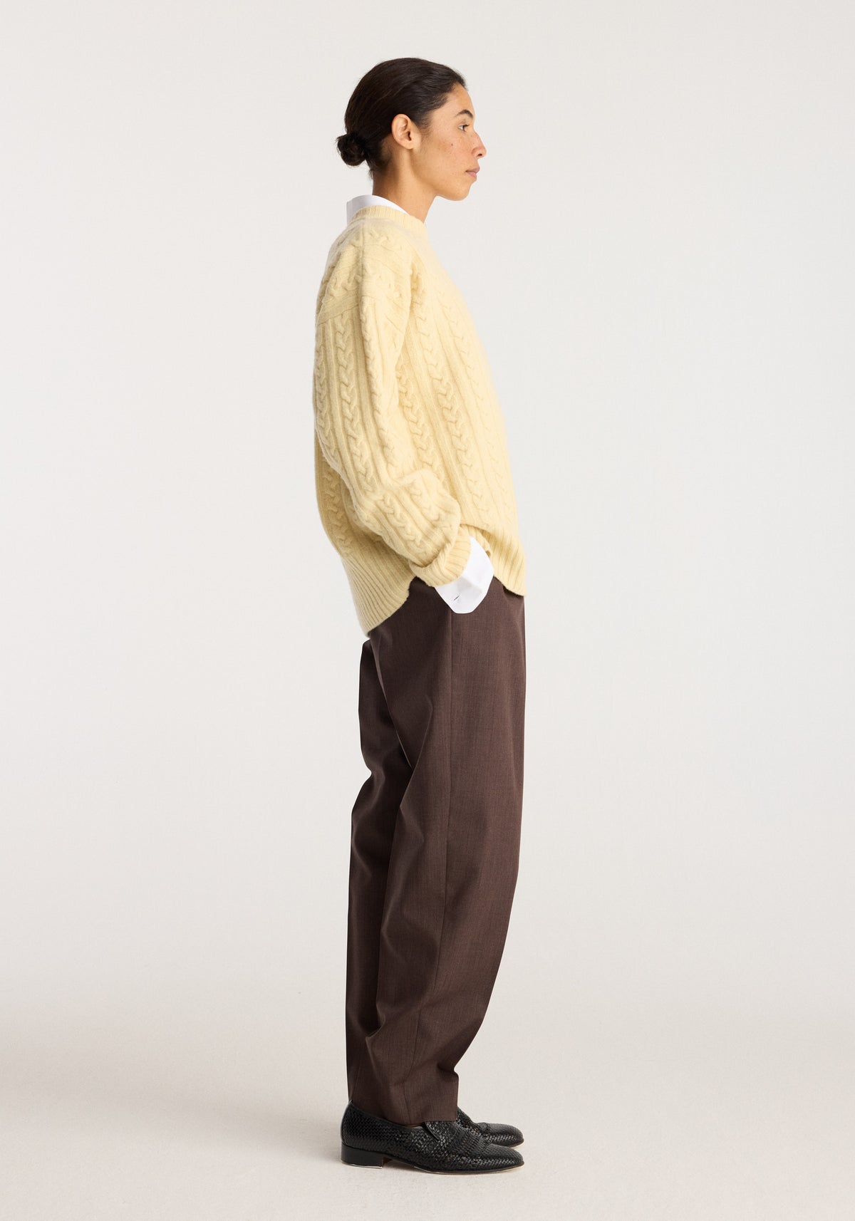 Cable knit jumper | butter shown in side profile on a model with relaxed brown trousers and black shoes against a light neutral background