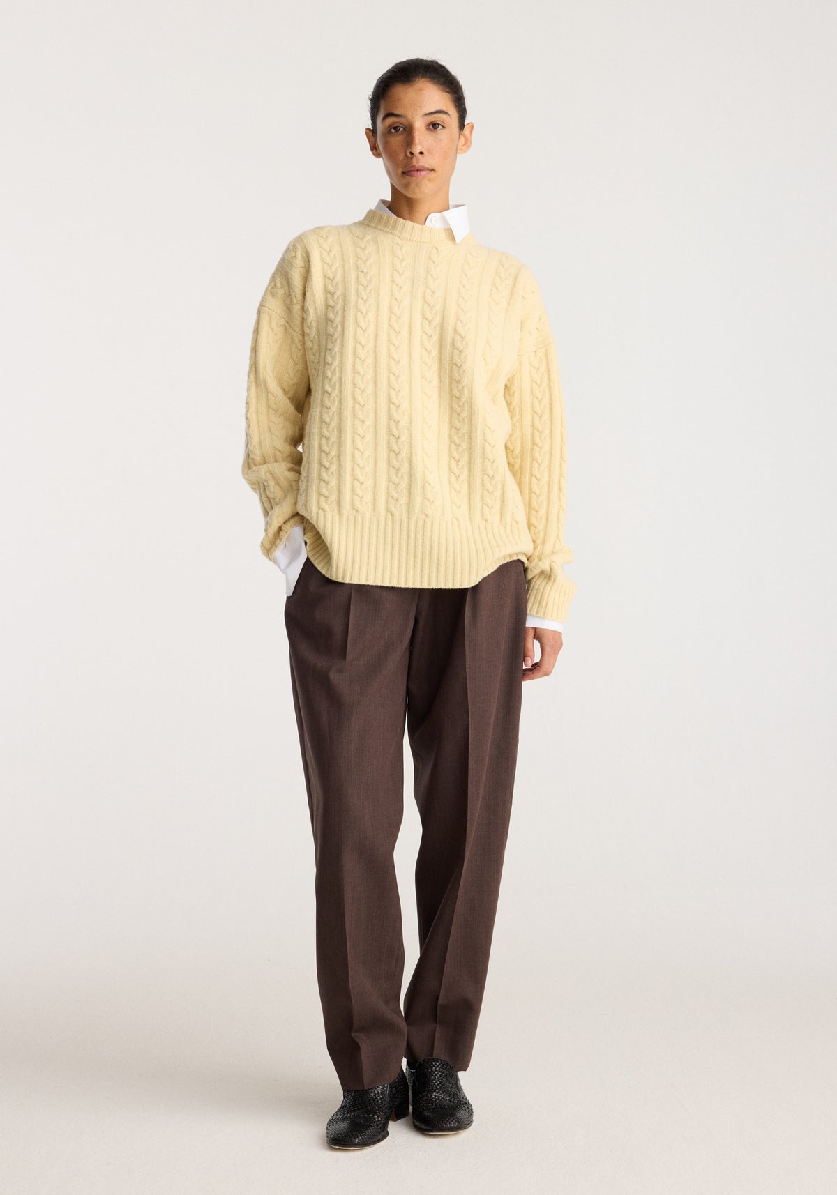 Cable knit jumper | butter worn with brown trousers and black shoes, featuring a textured cable knit design and relaxed fit on a standing model