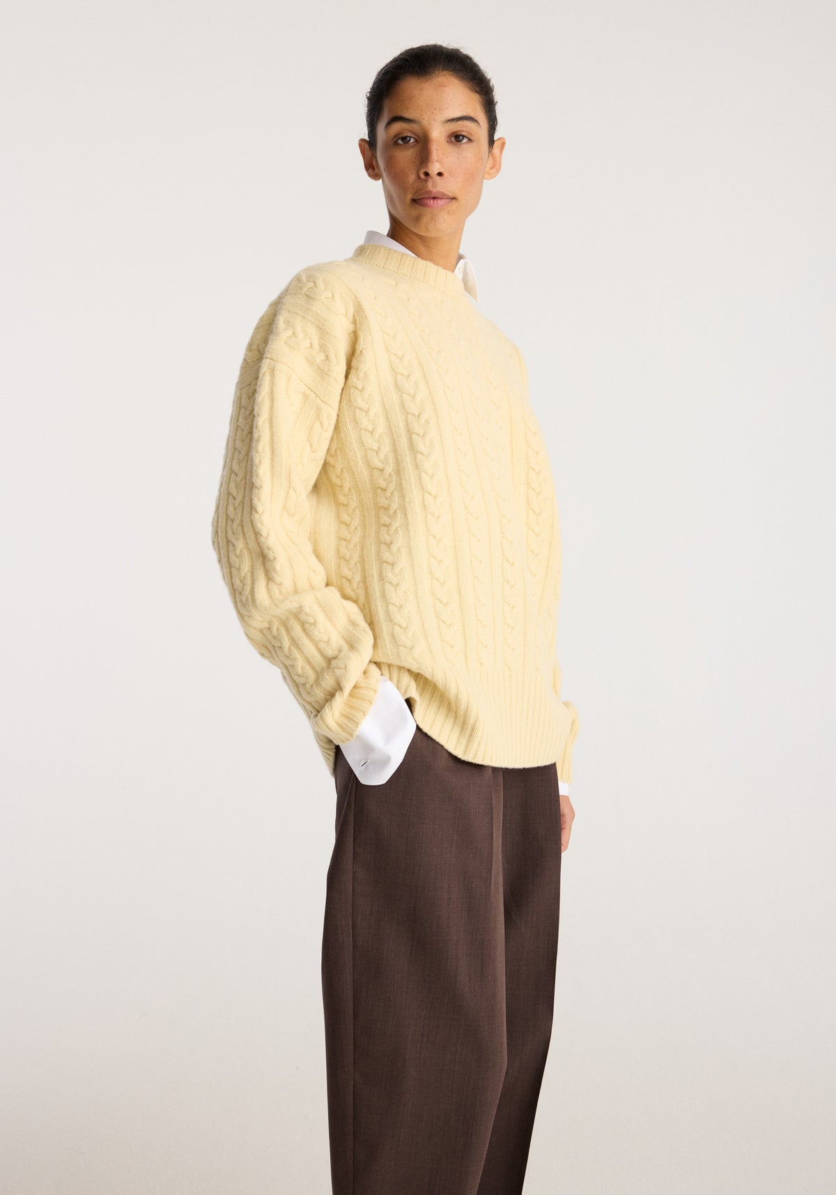 Cable knit jumper | butter shown on a model with cable detailing and ribbed cuffs styled with brown trousers against a neutral studio background