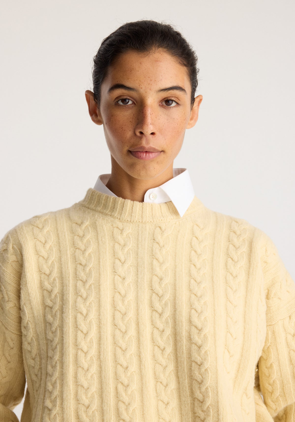 Cable knit jumper | butter in a soft butter yellow shade with vertical cable knit texture worn over a white collared shirt by a model