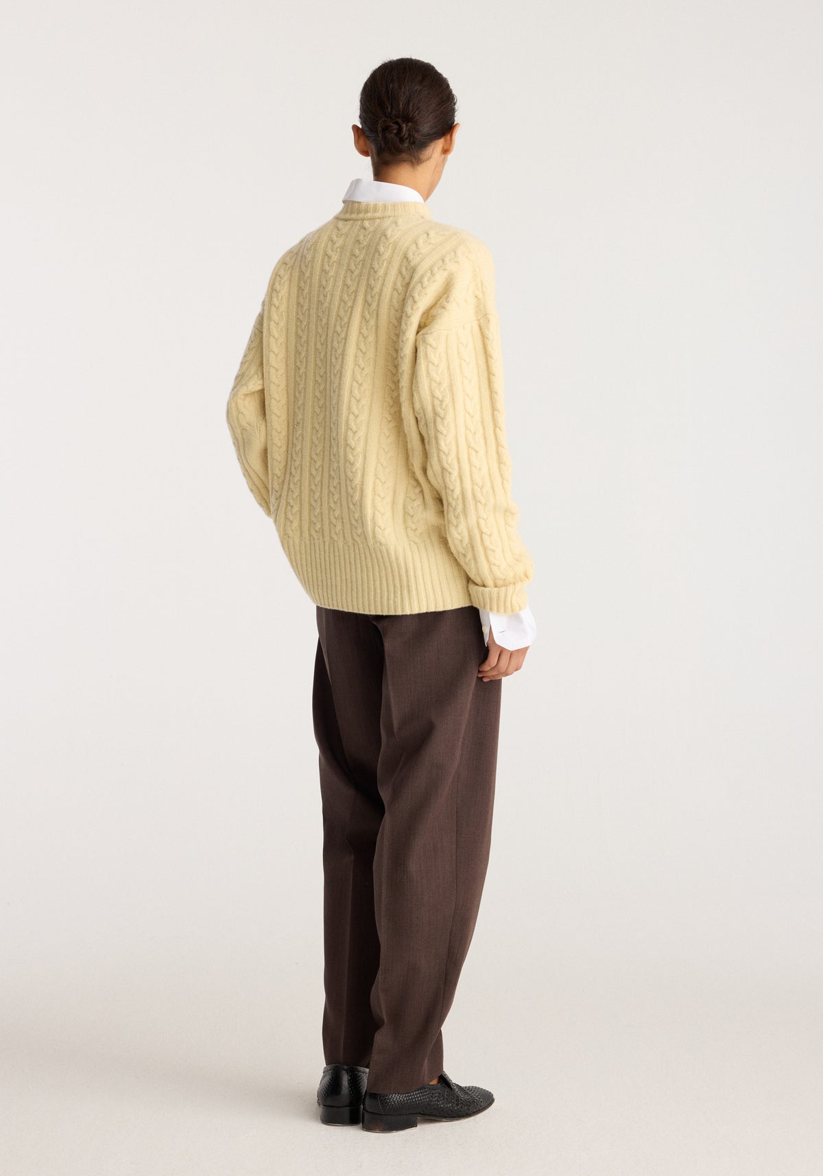 Cable knit jumper | butter seen from the back on a model with textured cable knit detailing and ribbed hems styled with dark brown trousers