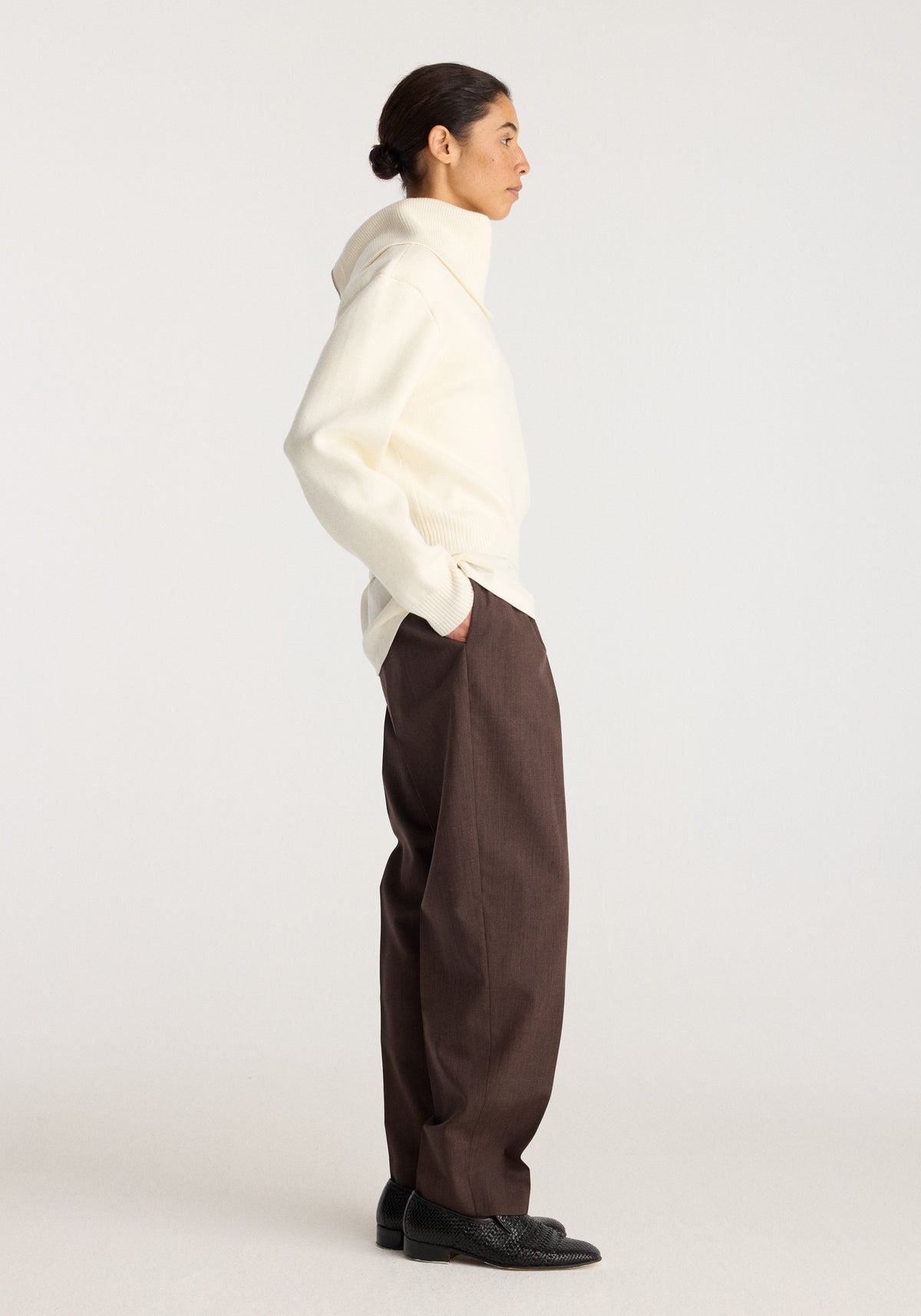 Reversible sailor zip cardigan | cream worn by a model in profile with relaxed brown trousers and black shoes on a neutral studio background