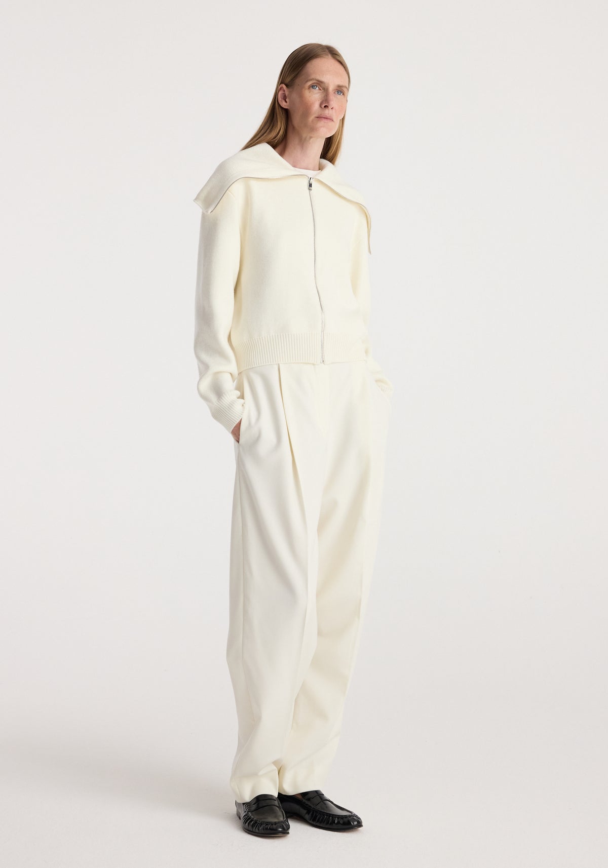 Woman wearing a cream zip-up cardigan with a sailor collar and matching cream wide-leg pants, styled with black shoes, standing against a plain background in Two way sailor zip cardigan | cream.
