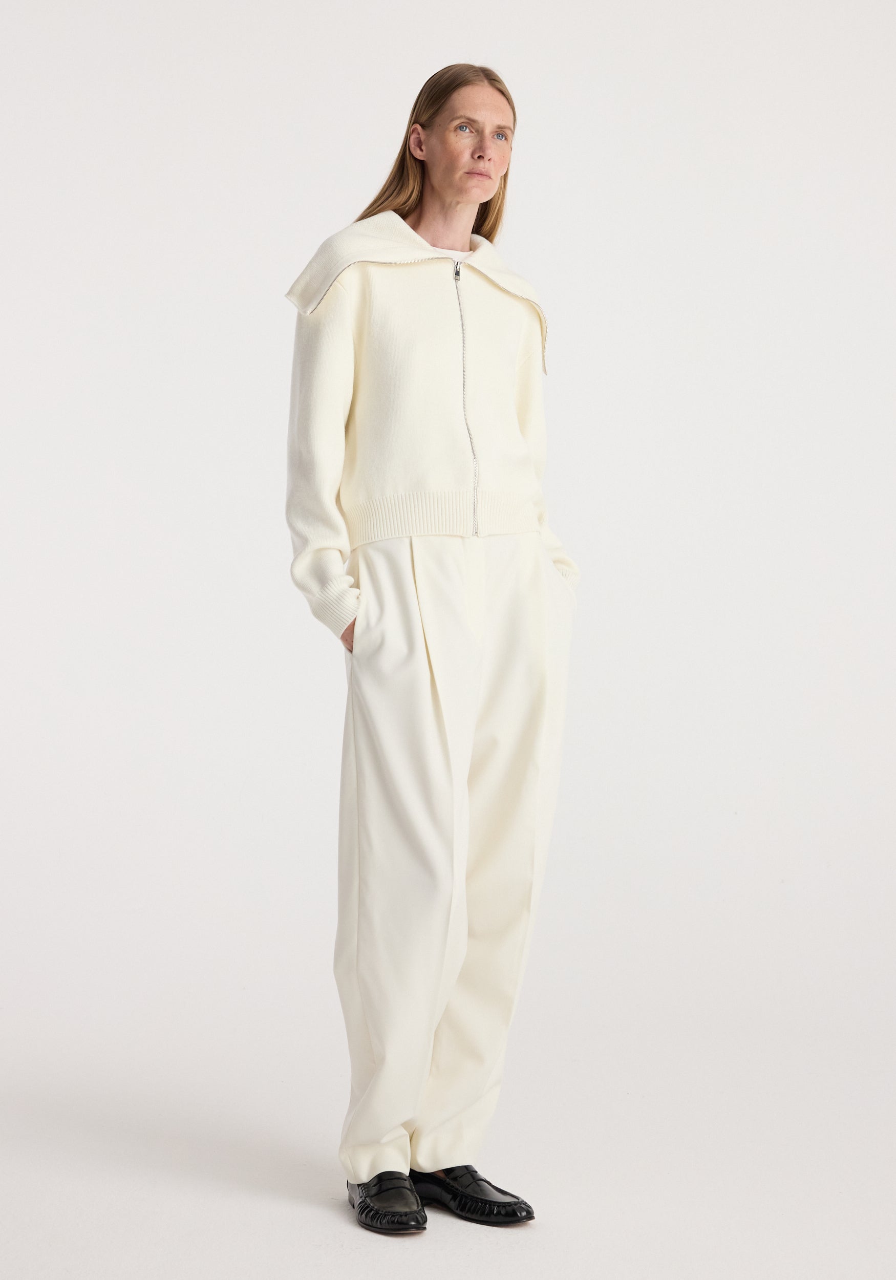 Woman wearing a cream zip-up cardigan with a sailor collar and matching cream wide-leg pants, styled with black shoes, standing against a plain background in Two way sailor zip cardigan | cream.