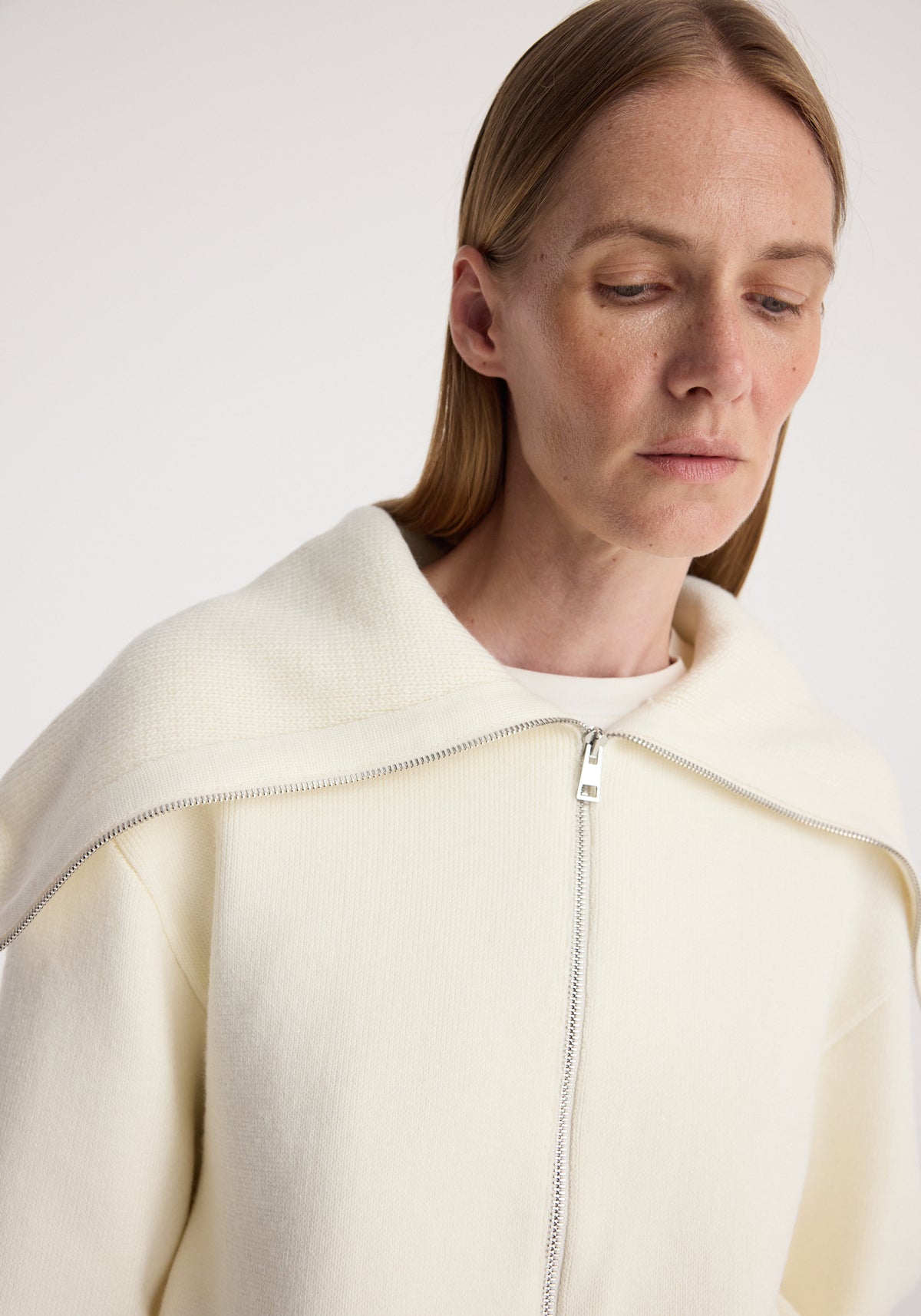 Close-up of a woman wearing a cream Two way sailor zip cardigan | cream with a partially unzipped collar detail and a soft textured fabric.