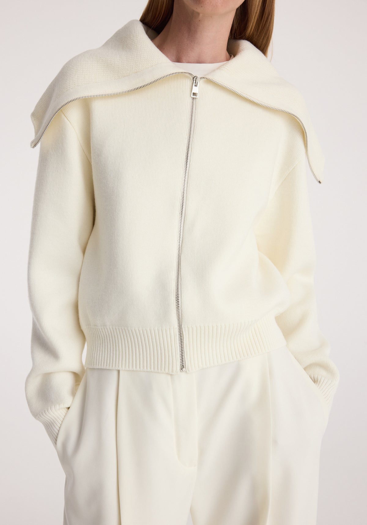 Woman wearing a cream knit zip-up cardigan with a wide sailor collar draped over the shoulders and matching cream pants, styled casually with hands in pockets, Two way sailor zip cardigan | cream.