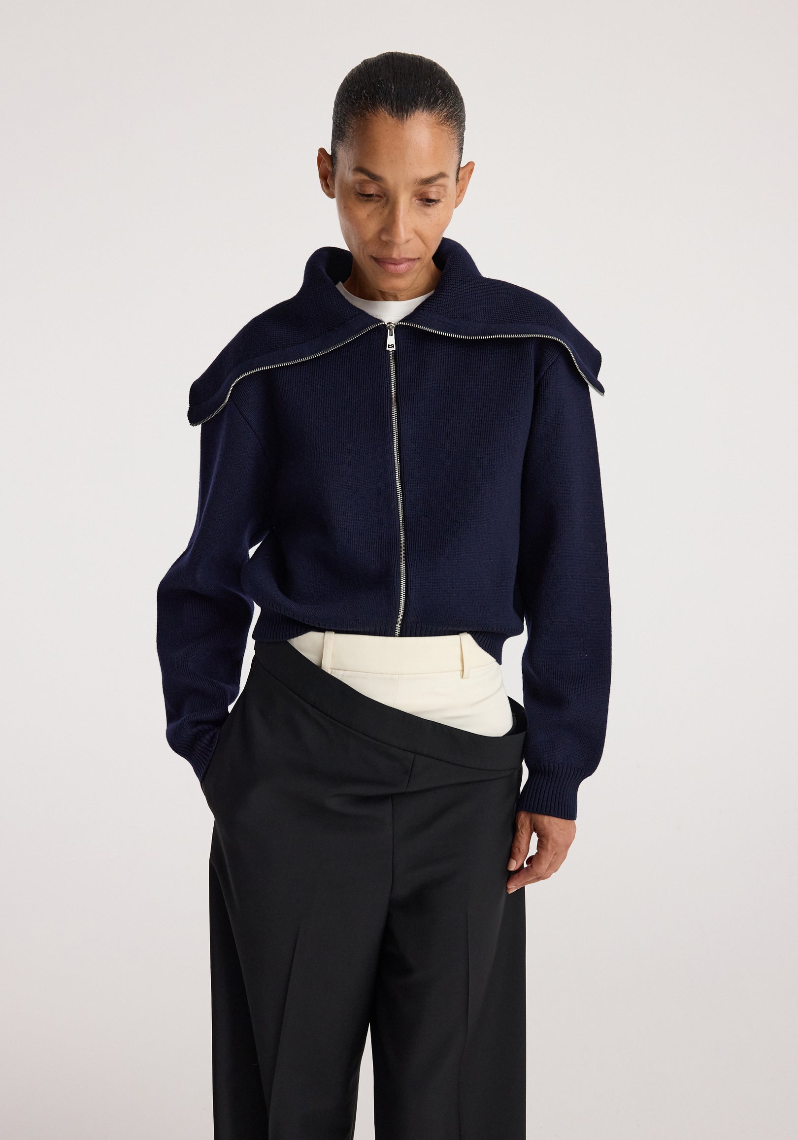 Woman wearing a navy zip-up cardigan with a unique sailor collar, styled with beige and black pants, showcasing the Two way sailor zip cardigan | navy.
