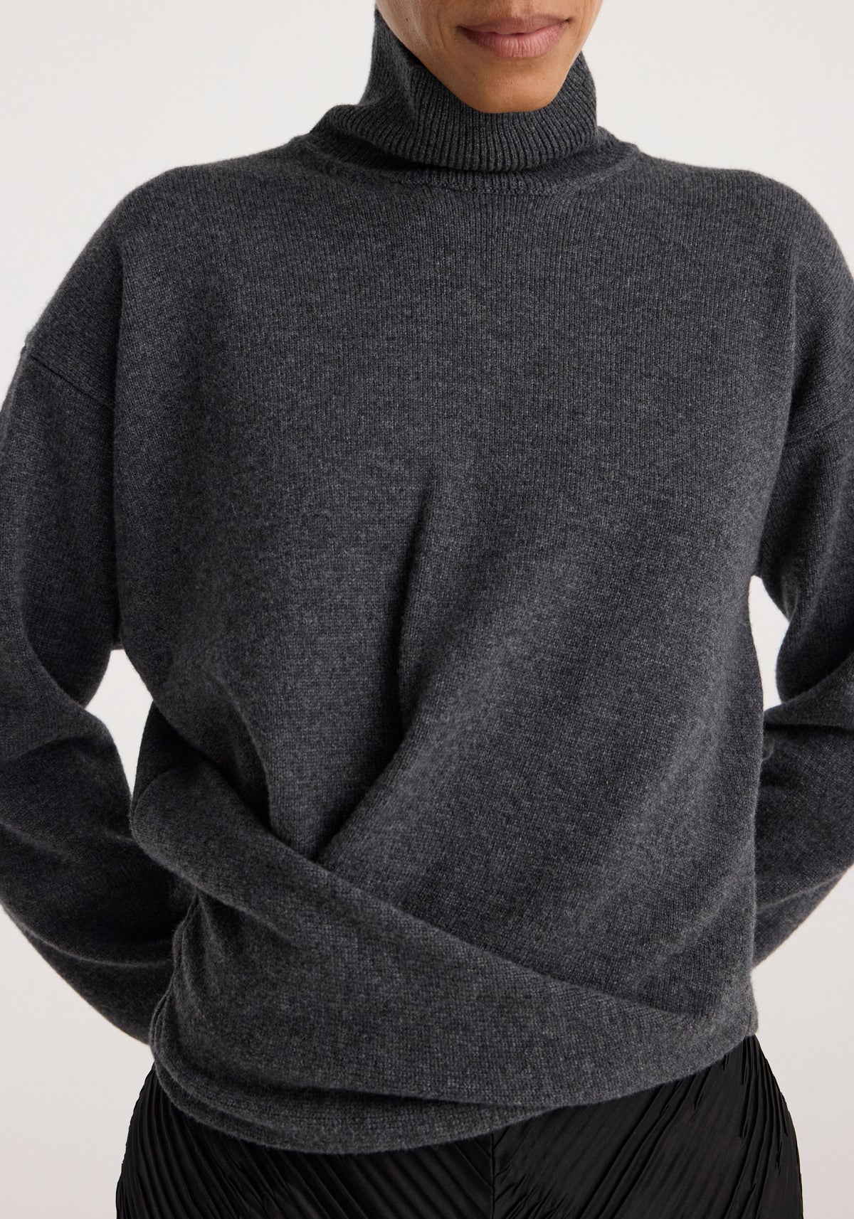 Close-up of a person wearing a Sculptural turtleneck | dark grey melange, featuring a soft, textured knit and a high, ribbed turtleneck collar.