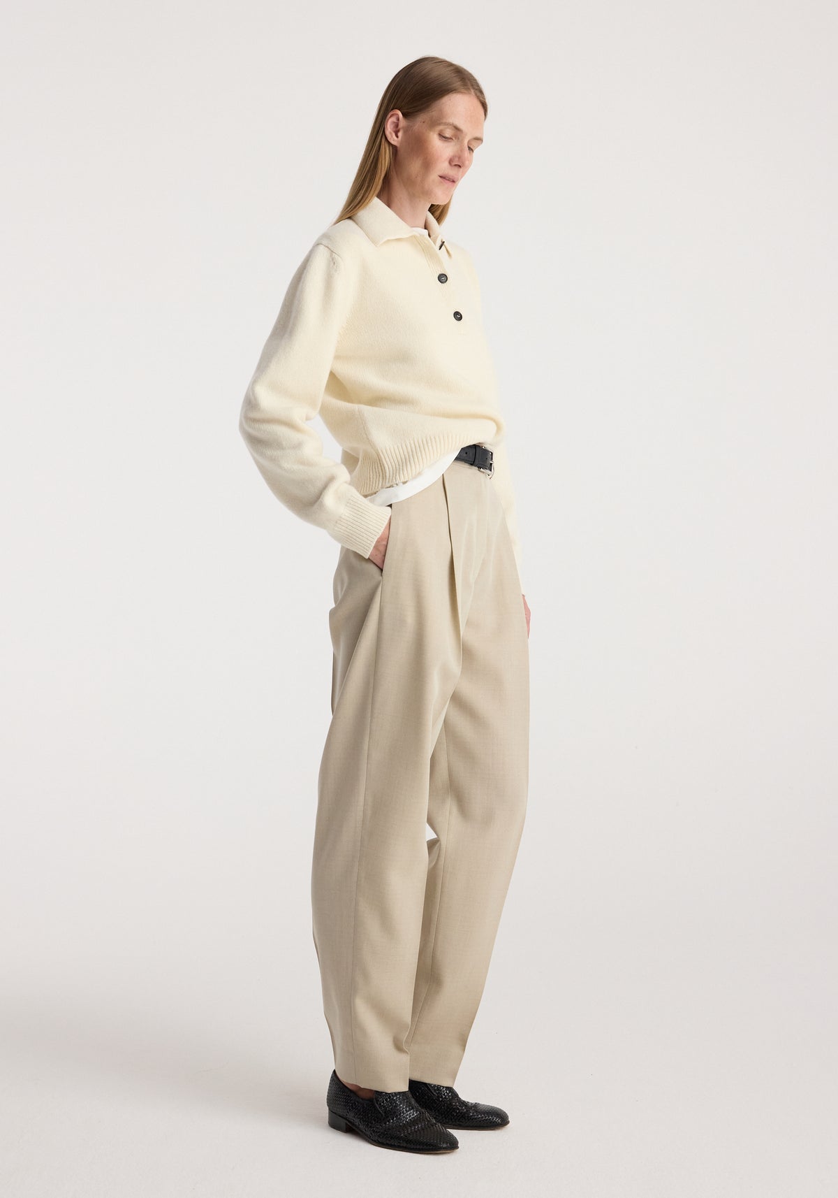 Wool-cashmere polo | cream worn by a woman with cream pleated trousers and black shoes in a minimalist studio setting
