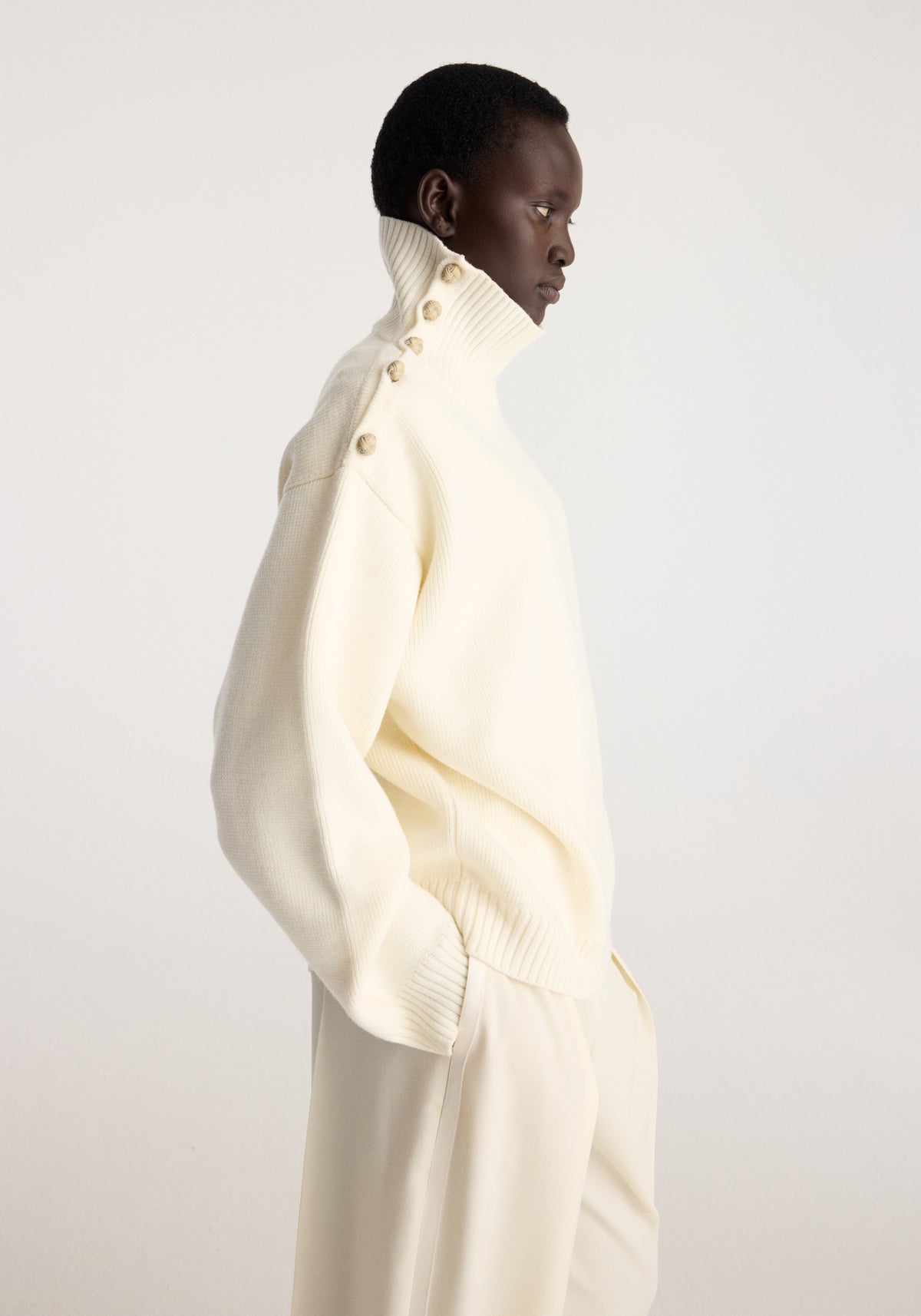 Uneven sailor polo | cream worn by a model in profile with a high neck button detail and relaxed fit in a light cream knit fabric