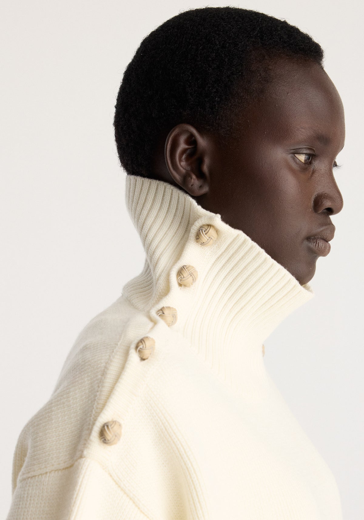 Uneven sailor polo | cream worn by a model in profile with a ribbed high neck and button details in a soft cream knit fabric