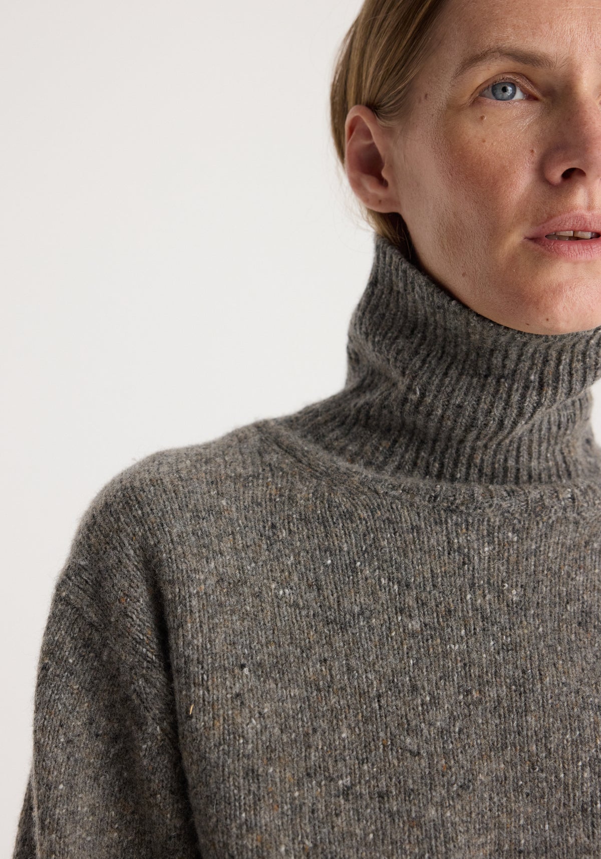 Close-up of a person wearing a grey textured knitted turtleneck sweater, showing the high ribbed collar and soft fabric of the Mouliné turtleneck | grey mouliné.