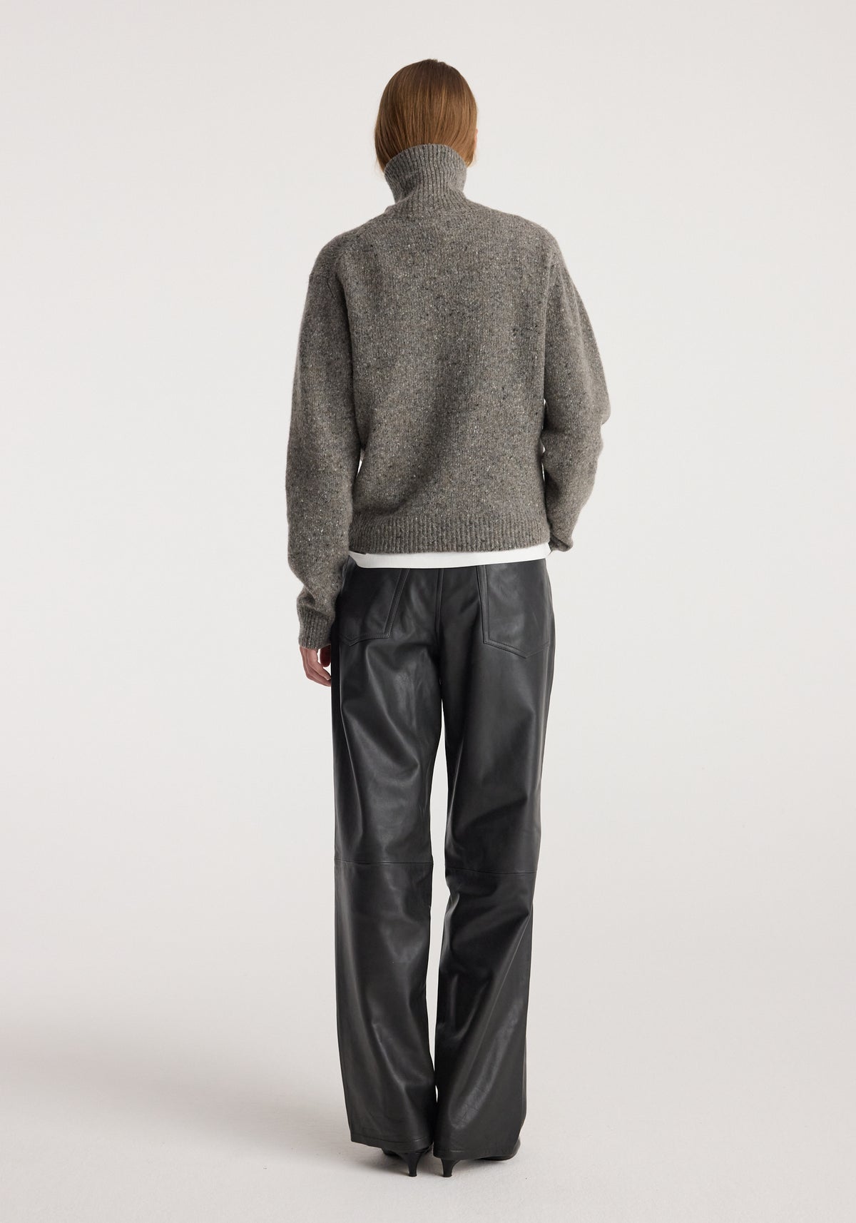 Woman seen from the back wearing a grey mouliné turtleneck with a high neck and long sleeves paired with black leather pants, showcasing the fit and texture of the Mouliné turtleneck | grey mouliné.