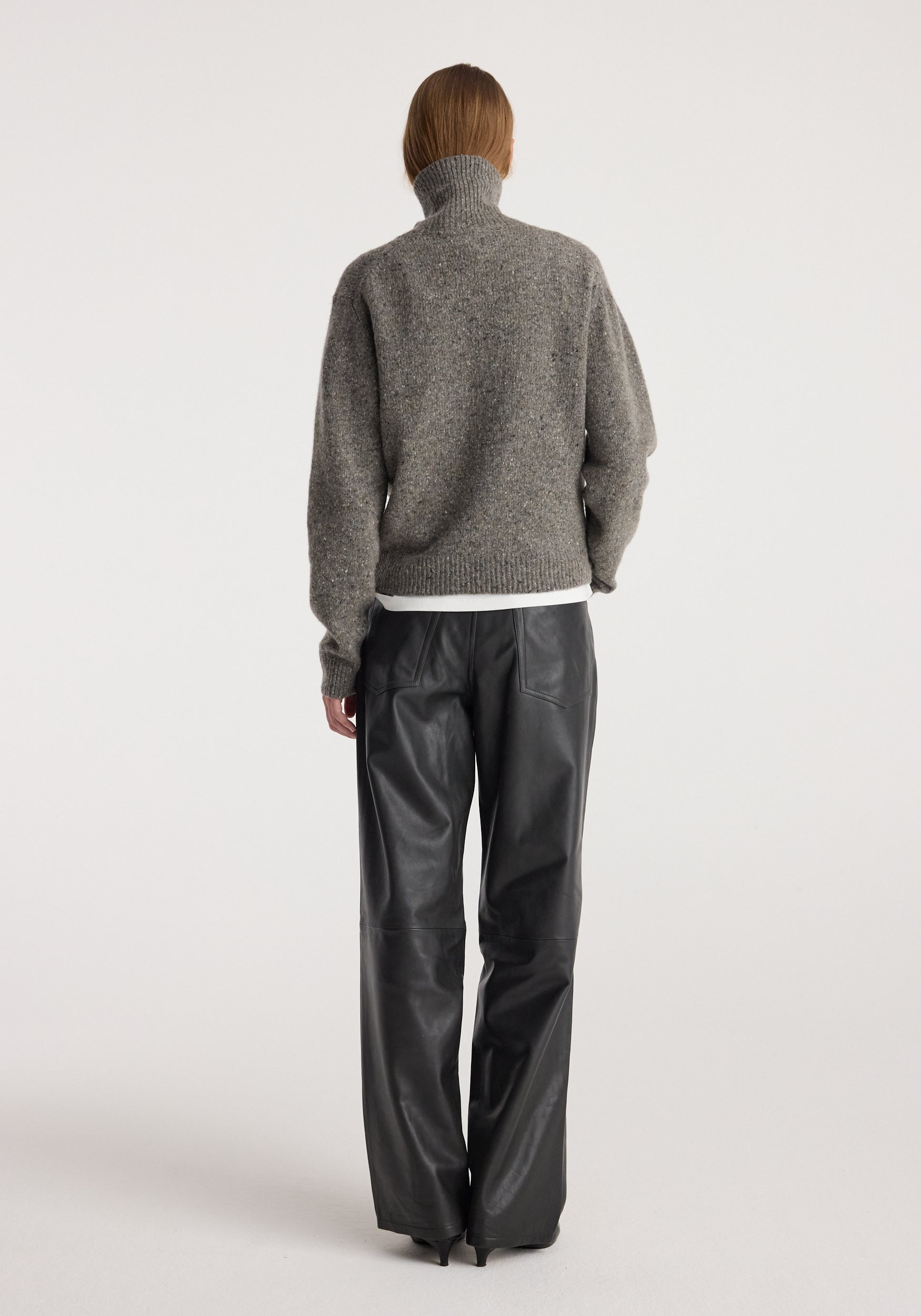Woman seen from the back wearing a grey mouliné turtleneck with a high neck and long sleeves paired with black leather pants, showcasing the fit and texture of the Mouliné turtleneck | grey mouliné.