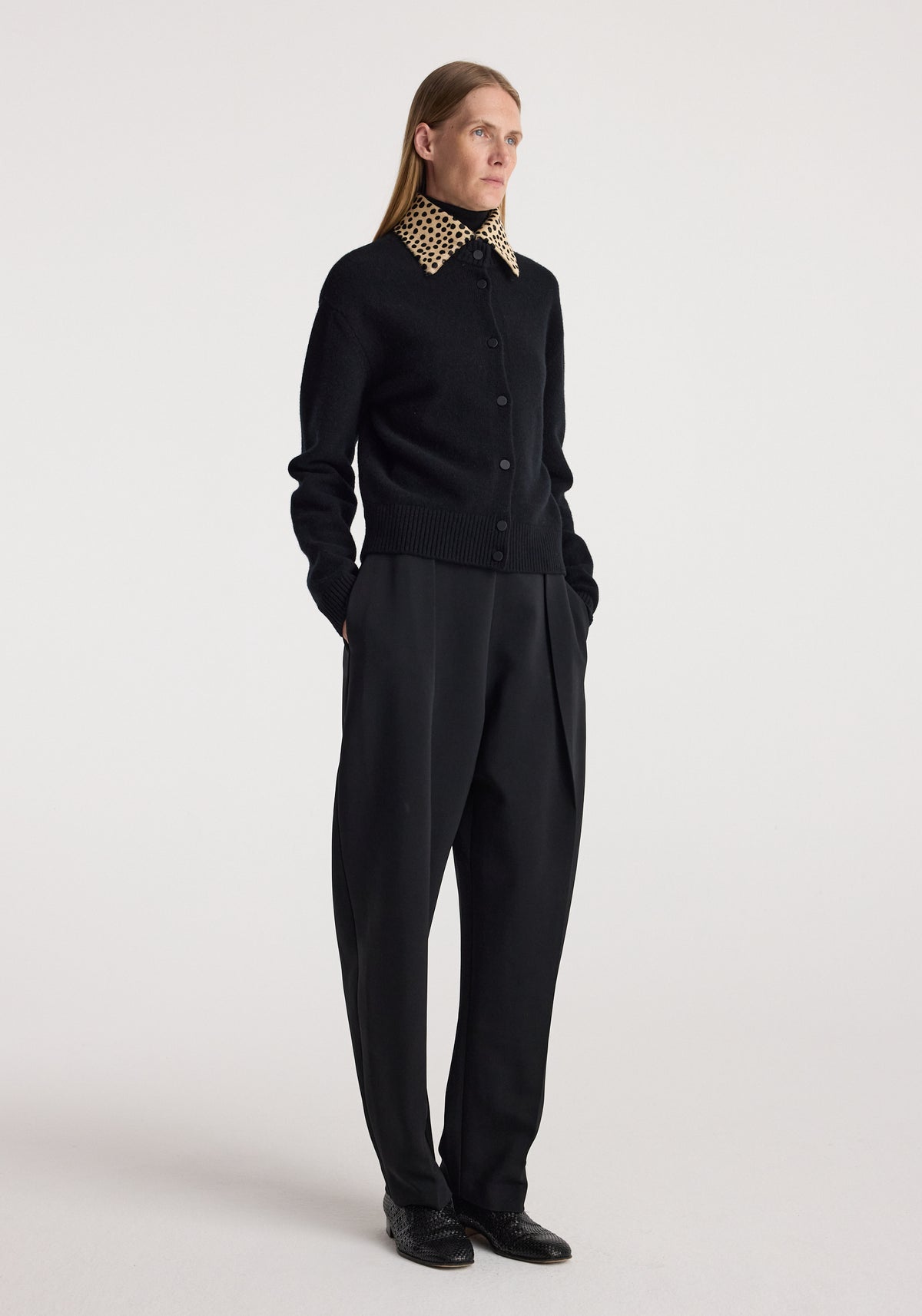 Woman wearing a black button-up sweater with a cheetah print collar, paired with loose black trousers and black shoes, styled in a minimal studio setting in the cheetah collar cardigan | black.