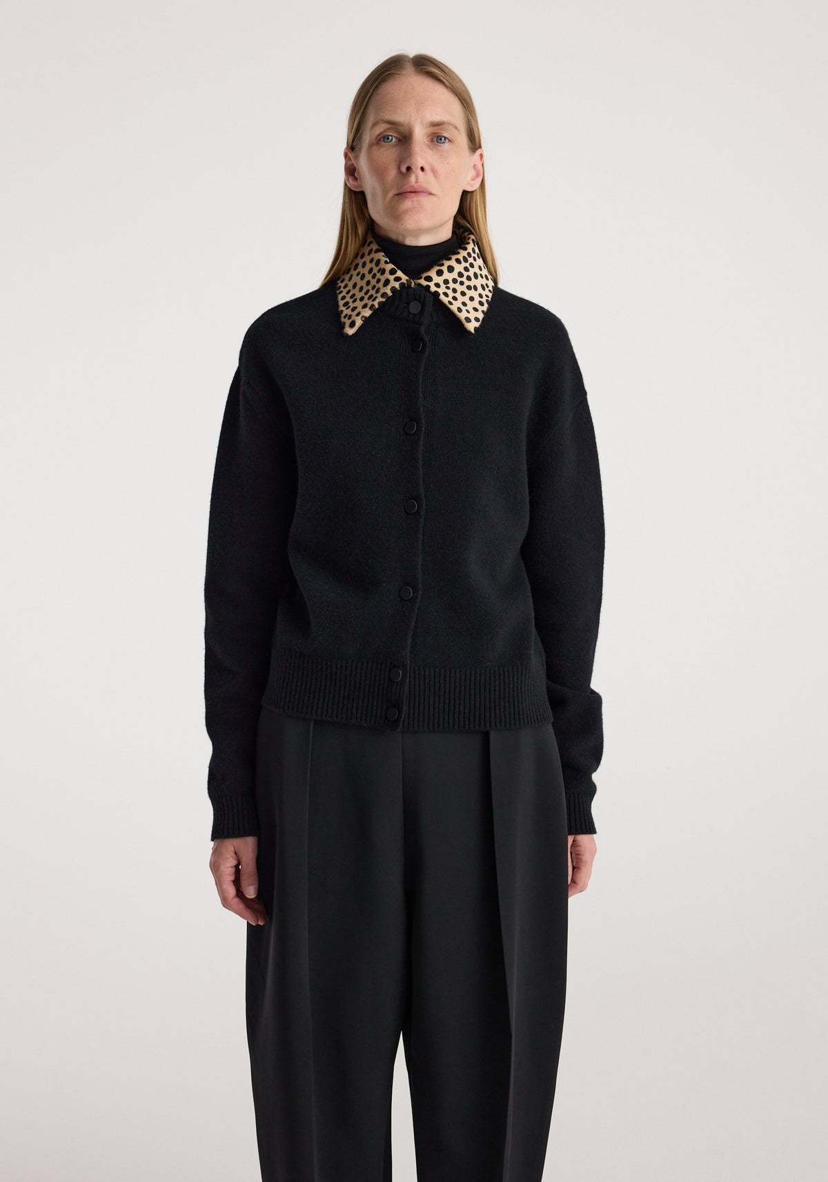 Woman wearing a black buttoned cardigan with a distinctive cheetah print collar paired with black wide-leg trousers, standing against a plain background, Cheetah collar cardigan | black.