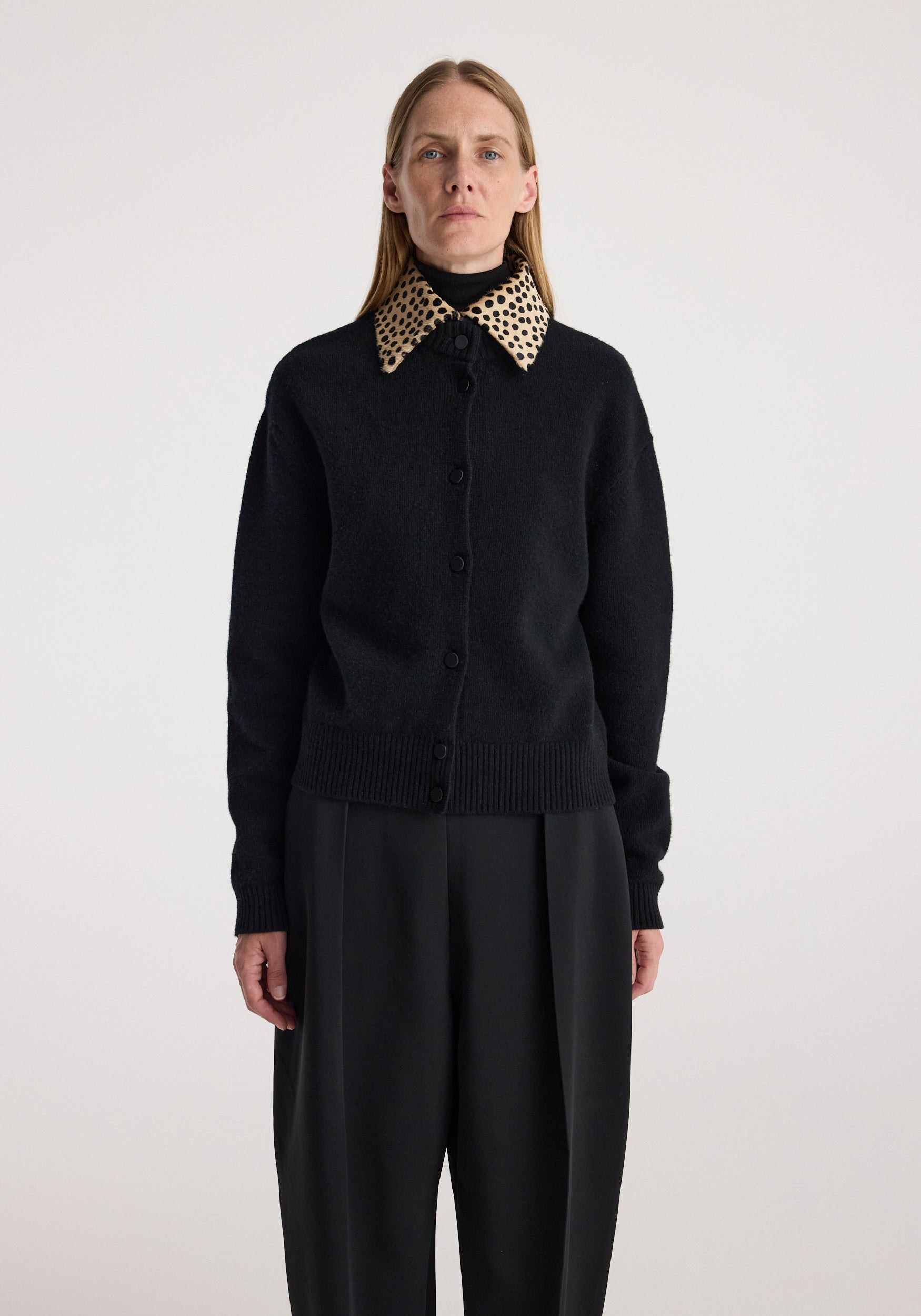 Woman wearing a black buttoned cardigan with a distinctive cheetah print collar paired with black wide-leg trousers, standing against a plain background, Cheetah collar cardigan | black.
