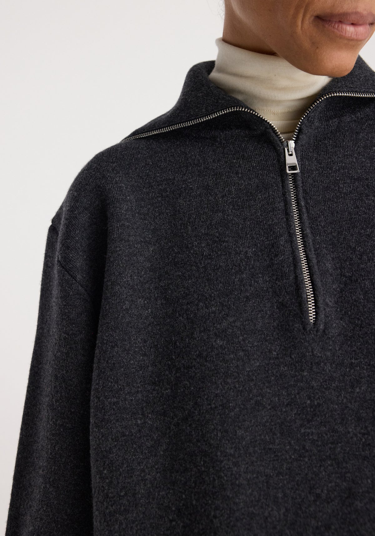 Close-up of a person wearing a charcoal Two-way zipped turtleneck | charcoal with a partially unzipped silver zipper and a white inner turtleneck underneath.