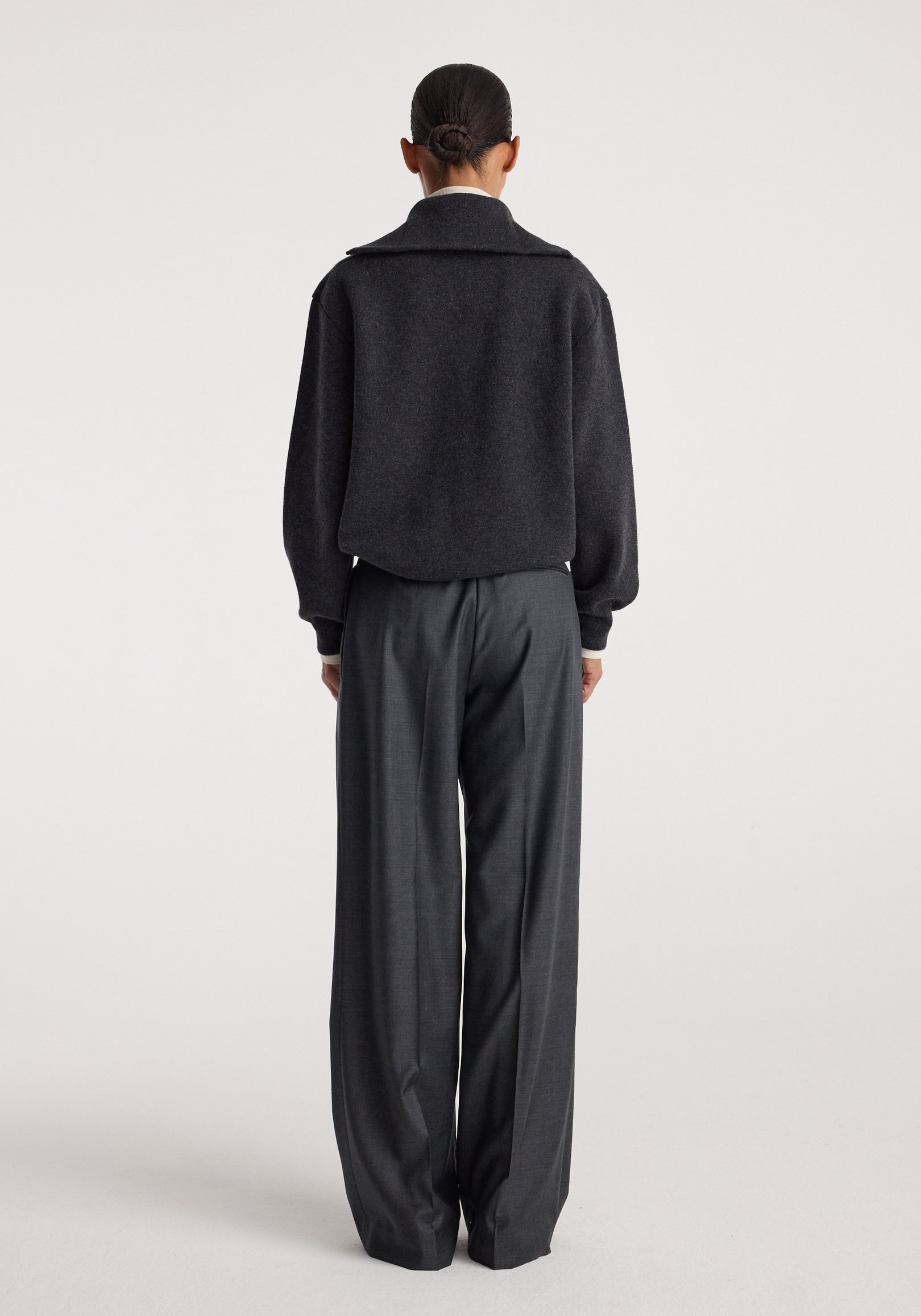 Rear view of a person wearing a charcoal Two-way zipped turtleneck with long sleeves, paired with loose-fitting dark gray trousers against a plain light background.