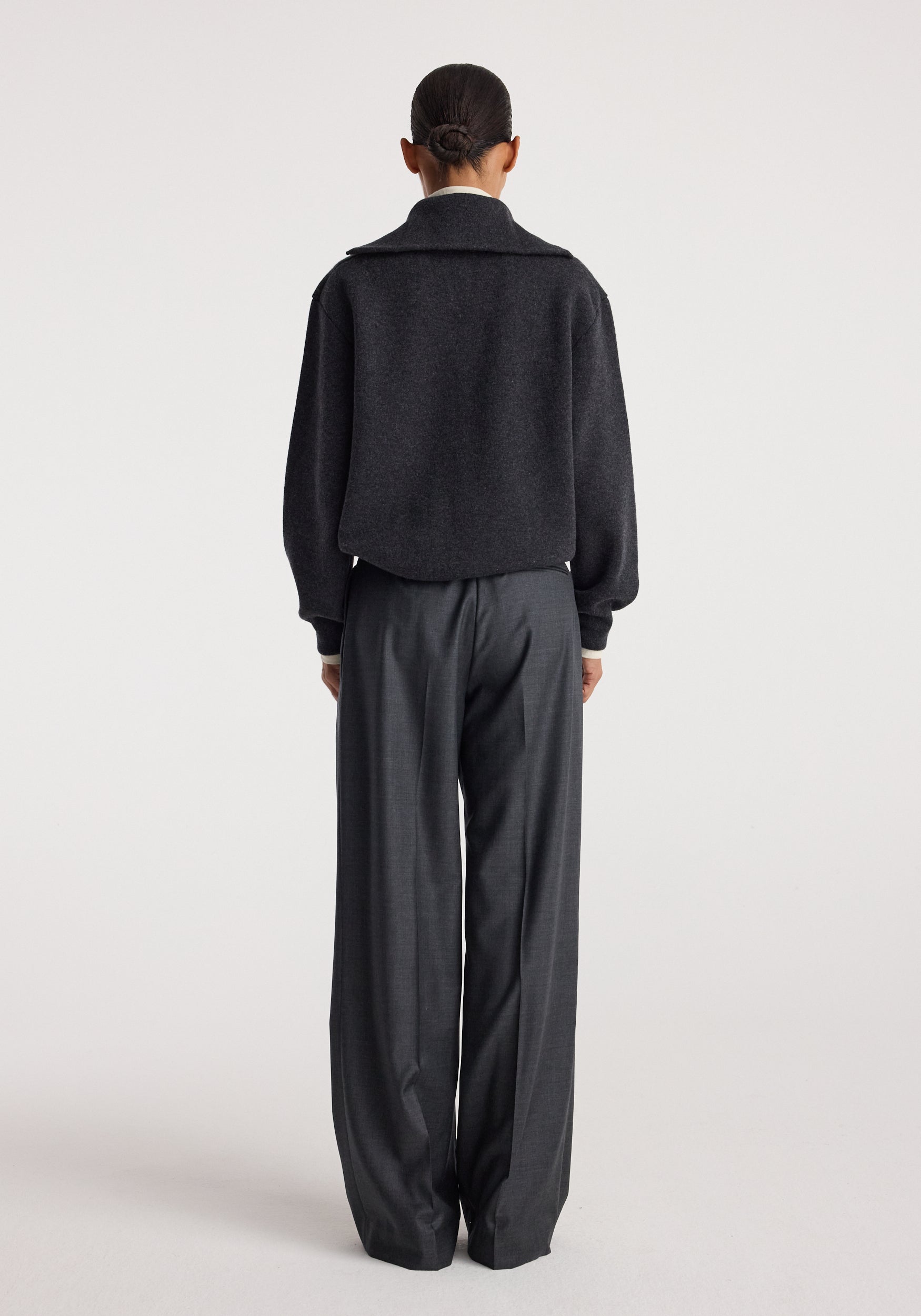 Rear view of a person wearing a charcoal Two-way zipped turtleneck with long sleeves, paired with loose-fitting dark gray trousers against a plain light background.
