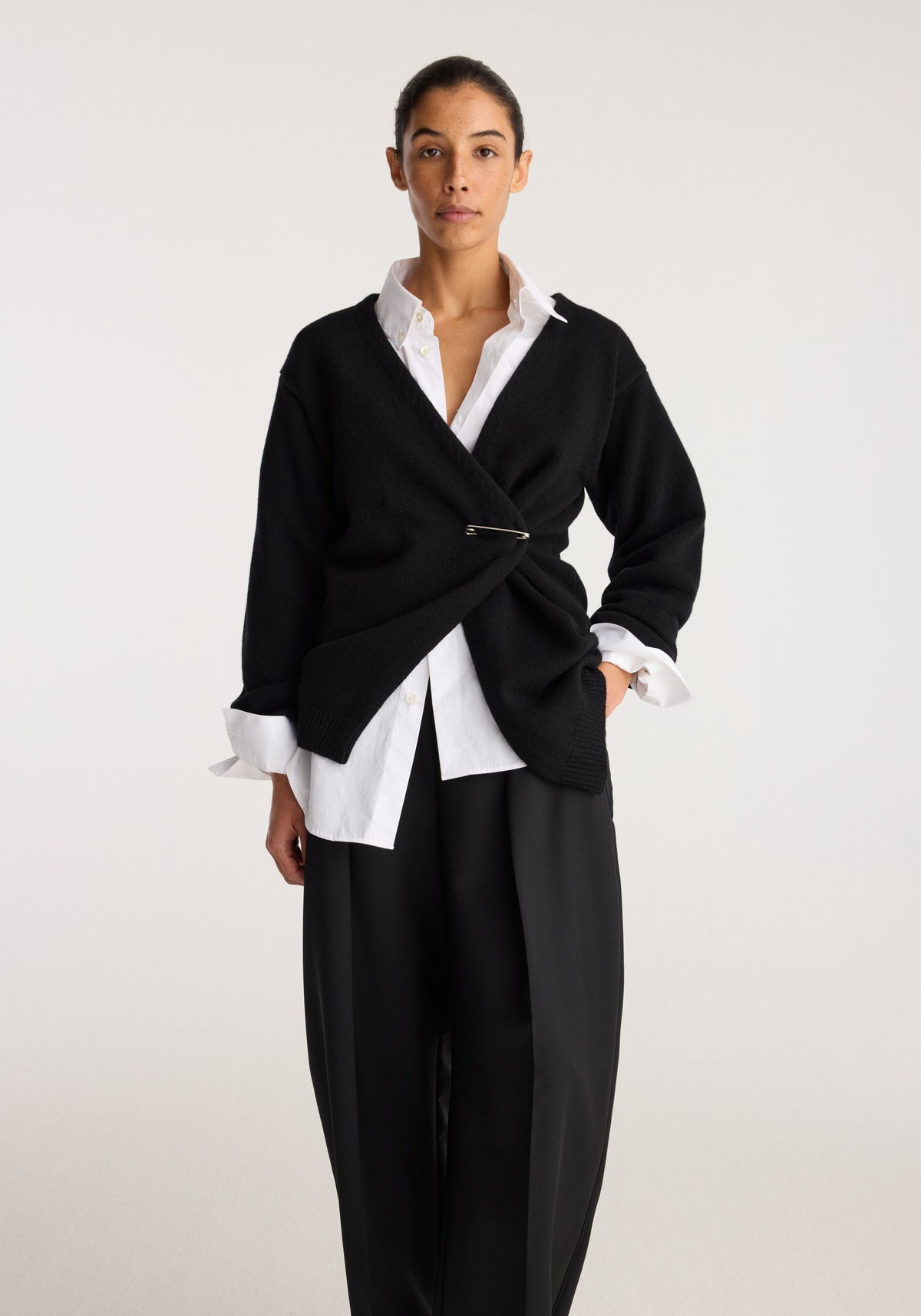 Off-shoulder wrap cardigan | black styled over a white shirt with wide-leg black trousers and a draped front with clasp fastening