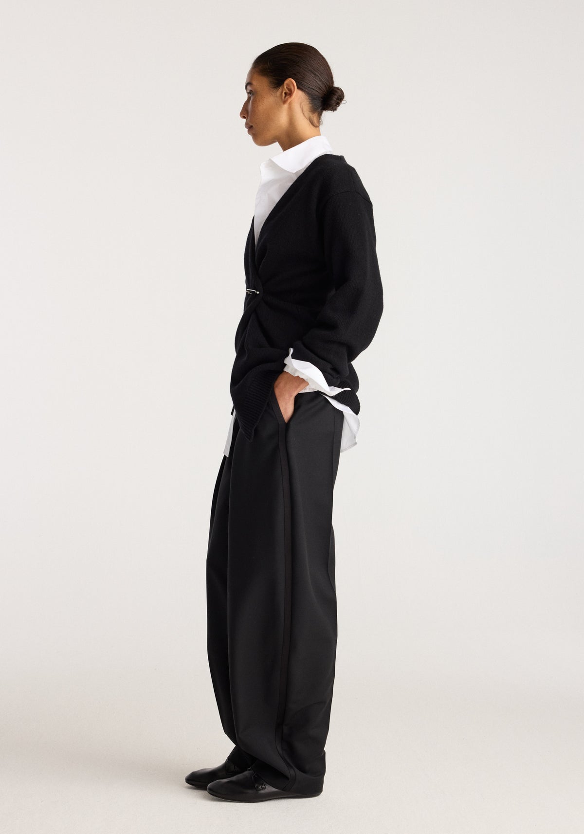 Off-shoulder wrap cardigan | black shown on a model in side profile with a white collared shirt and wide-leg black trousers