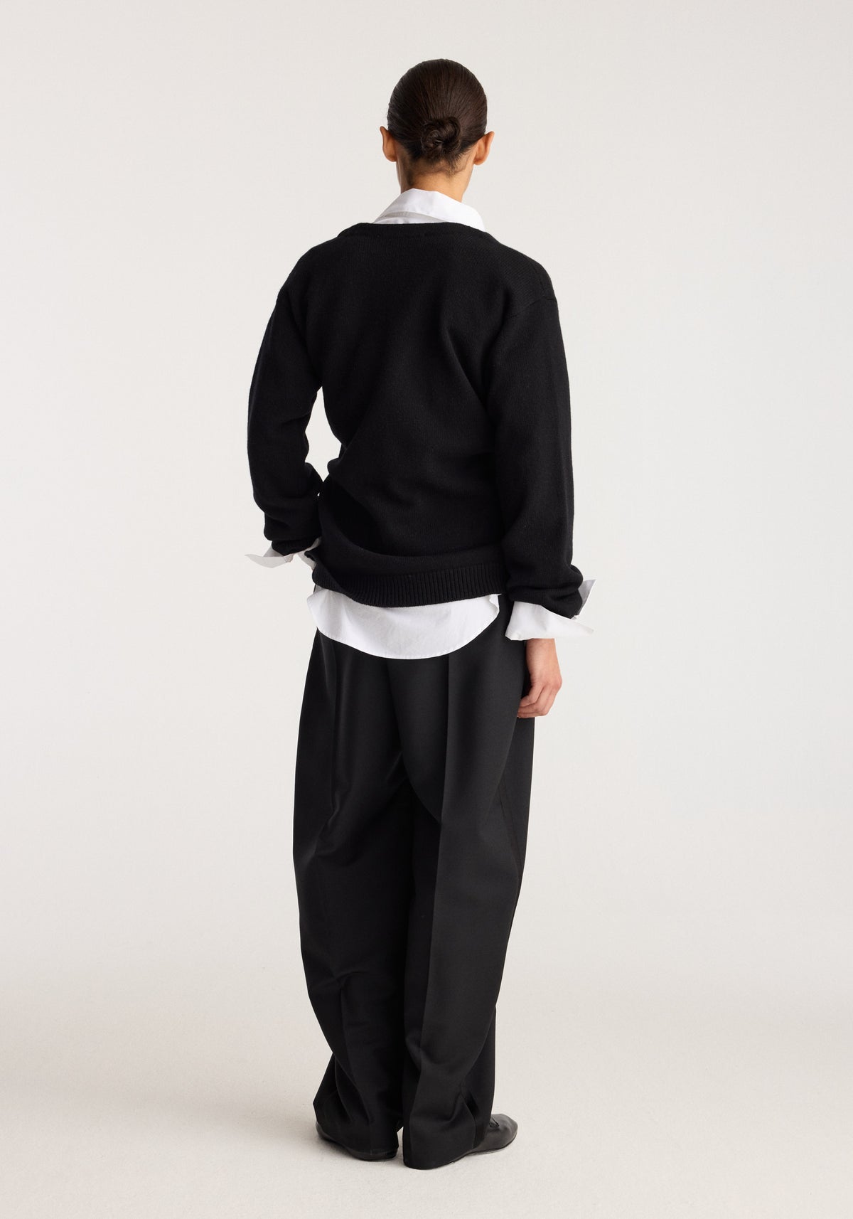 Off-shoulder wrap cardigan | black shown from the back on a model, layered over a white shirt with relaxed black trousers