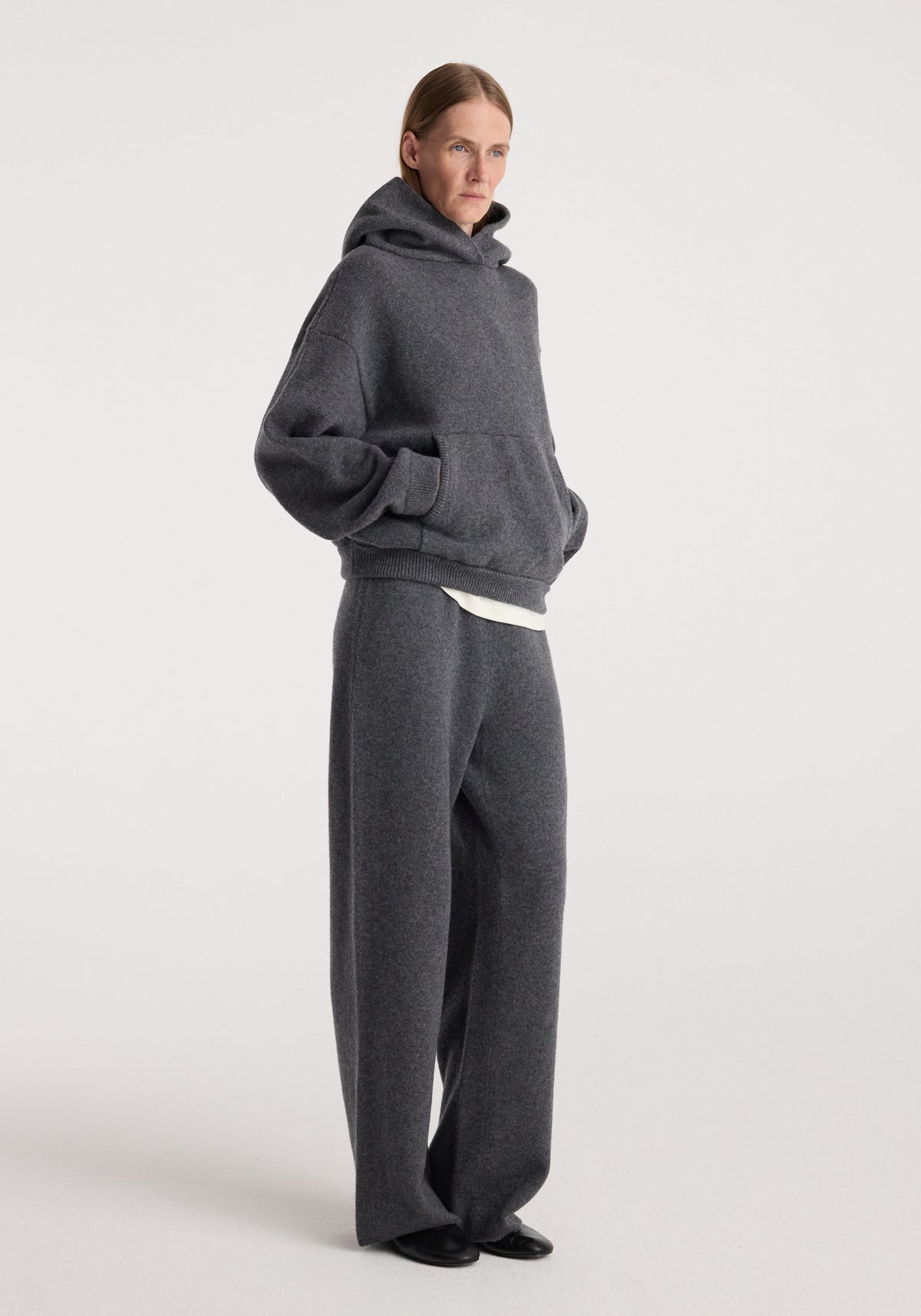 Model wearing the Hooded kangeroo jumper | dark grey melange, a relaxed charcoal hooded sweatshirt with kangaroo pocket and matching trousers.