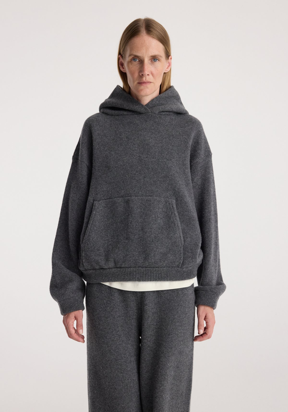 Model wearing Hooded kangeroo jumper | dark grey melange with a front kangaroo pocket and ribbed cuffs, styled with matching dark grey trousers