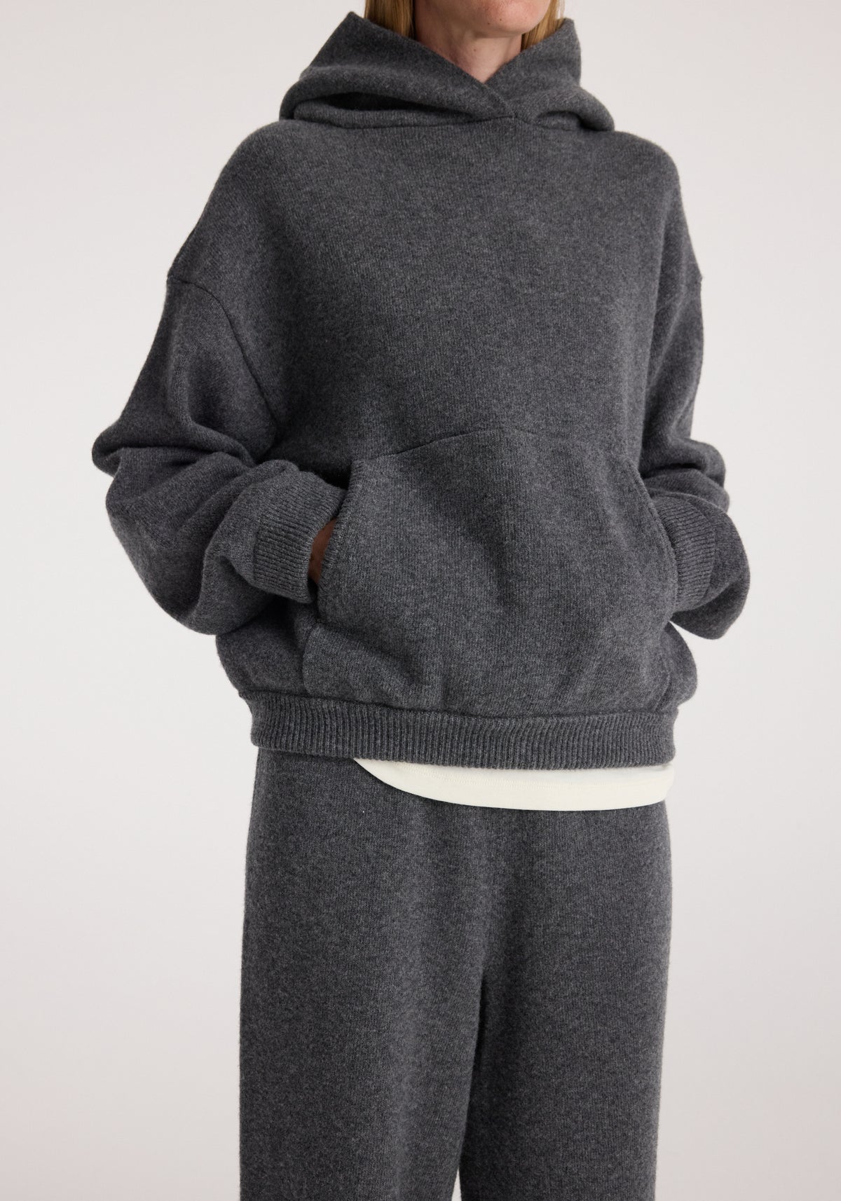 Hooded kangeroo jumper | dark grey melange worn by a model with hands in the front pouch pocket and matching dark grey trousers