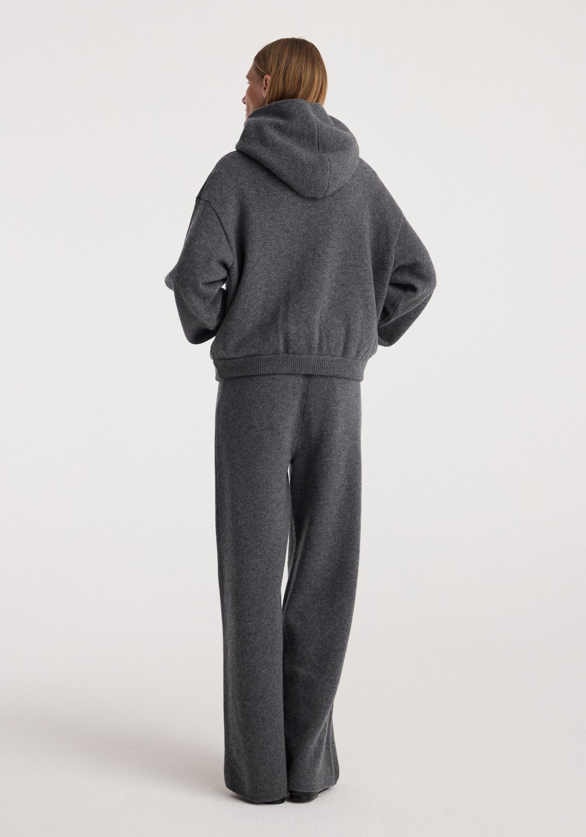 Back view of a model wearing Hooded kangeroo jumper | dark grey melange with a relaxed fit, hood, long sleeves and matching dark grey trousers against a neutral background
