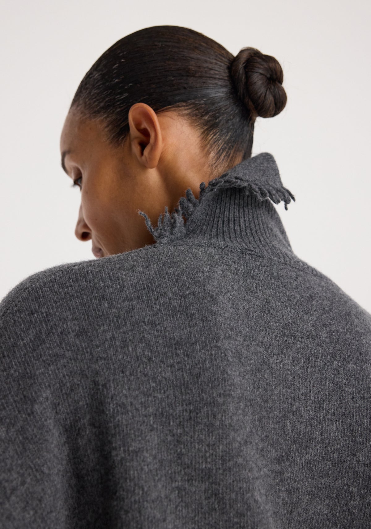 Close-up rear view of a person wearing a Turtleneck with raw details | dark grey melange, showcasing the textured fabric and unfinished collar edges.