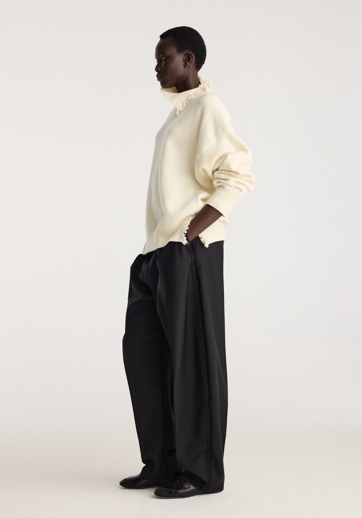 Turtleneck with raw details | off white worn by a model with black wide leg trousers in a minimalist studio setting