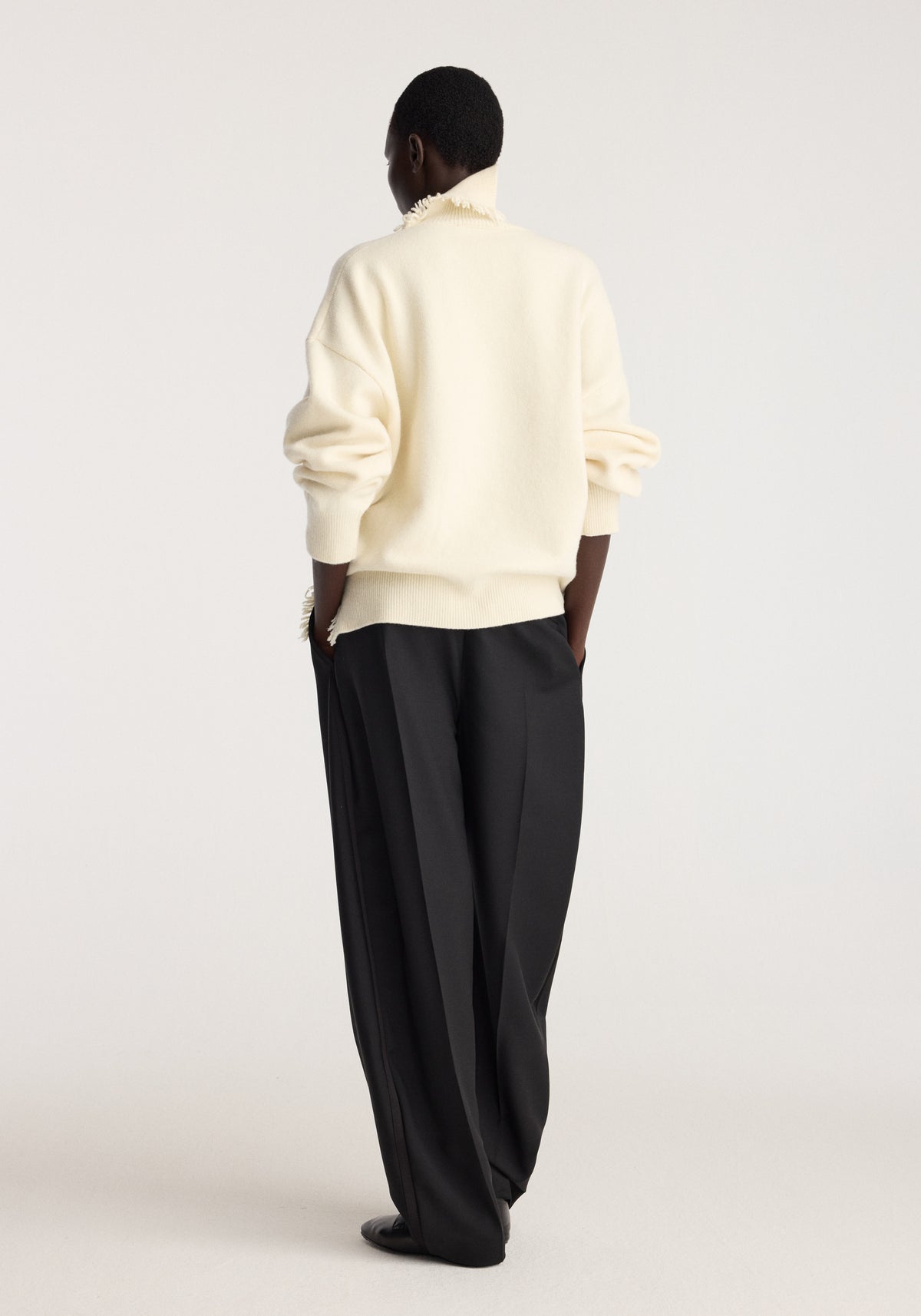 Turtleneck with raw details | off white shown from the back on a model with rolled sleeves, paired with relaxed black trousers in a minimalist studio setting